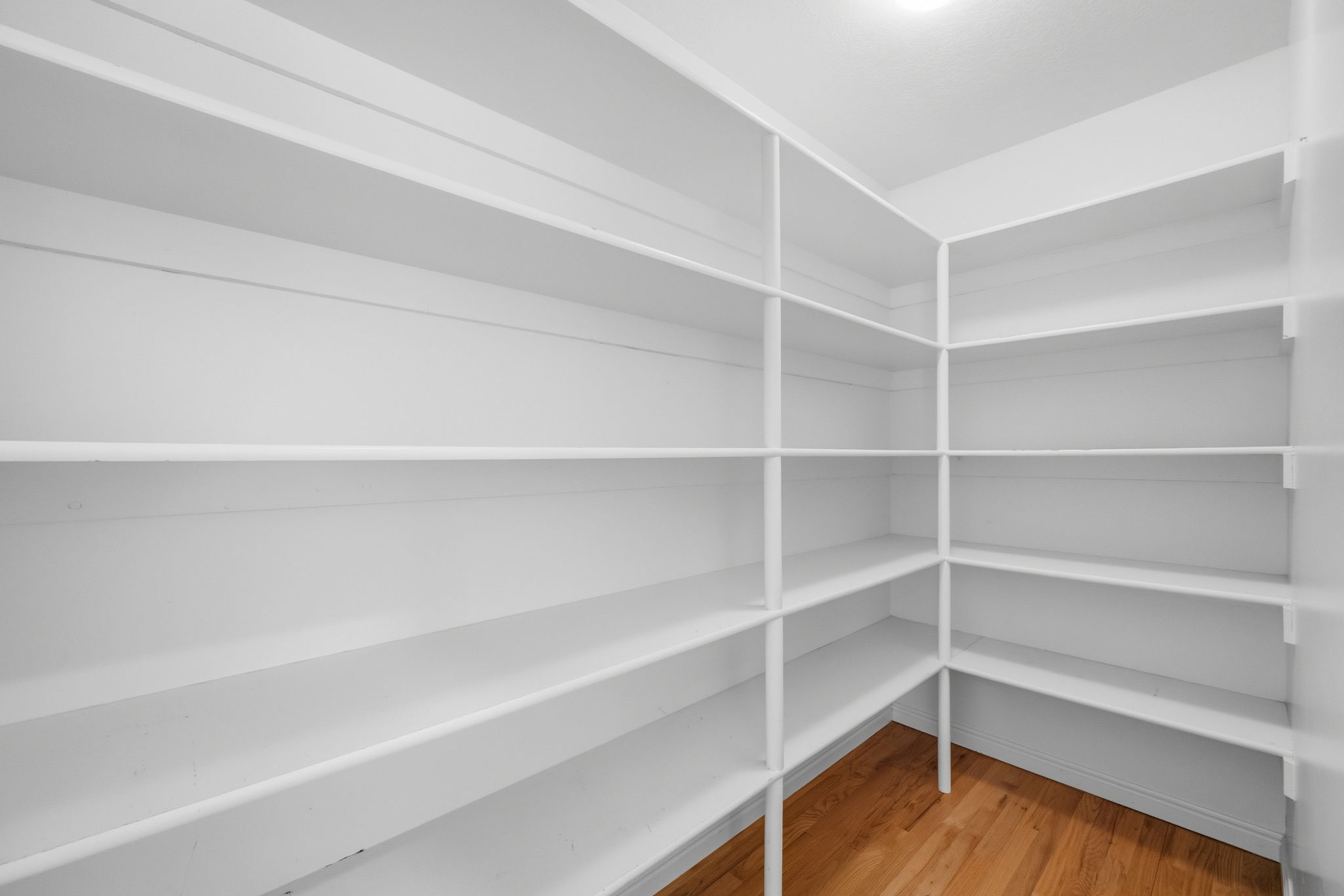 Walk-in pantry with extensive white shelving, hardwood flooring, and recessed ceiling lighting