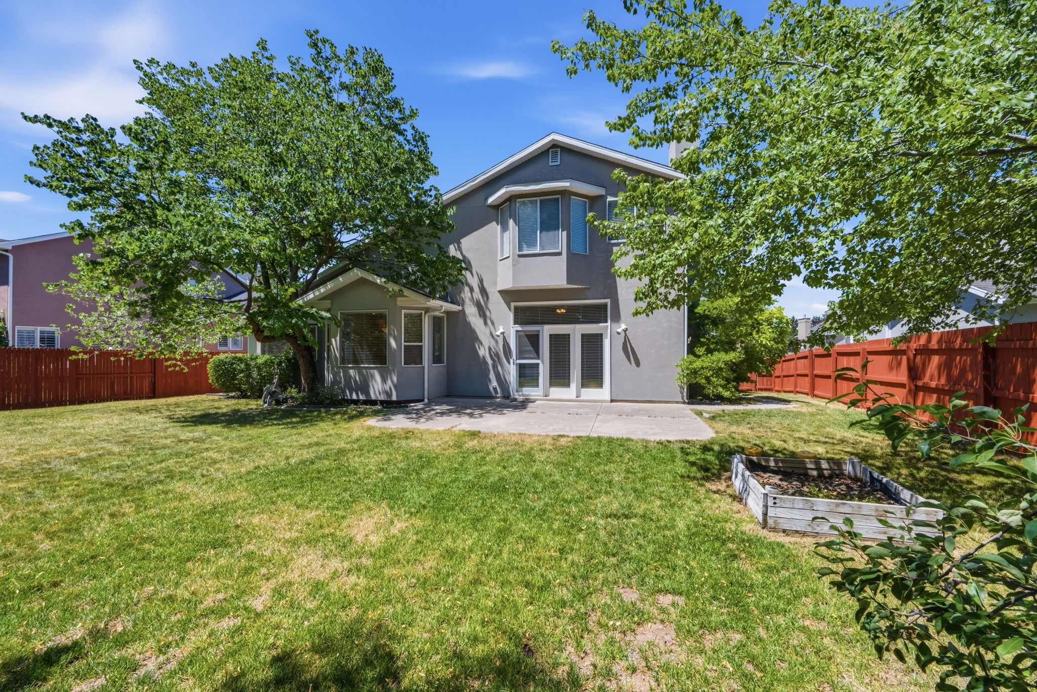 Expansive backyard featuring a manicured lawn, established trees, and a red privacy fence