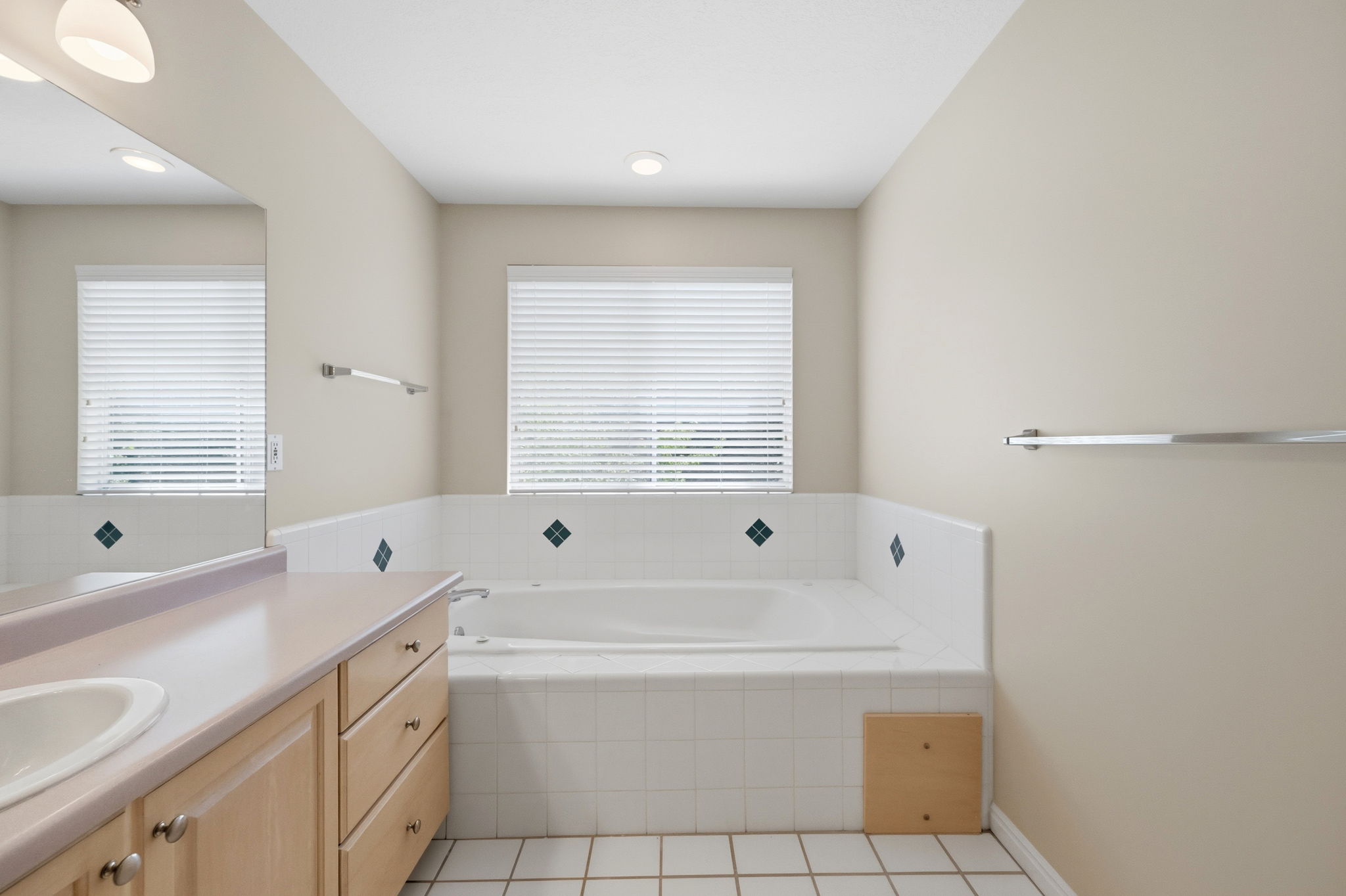 Bathroom featuring a built-in jetted tub with tile surround, a single vanity with an integrated sink and light wood cabinetry, a large wall mirror, and recessed lighting