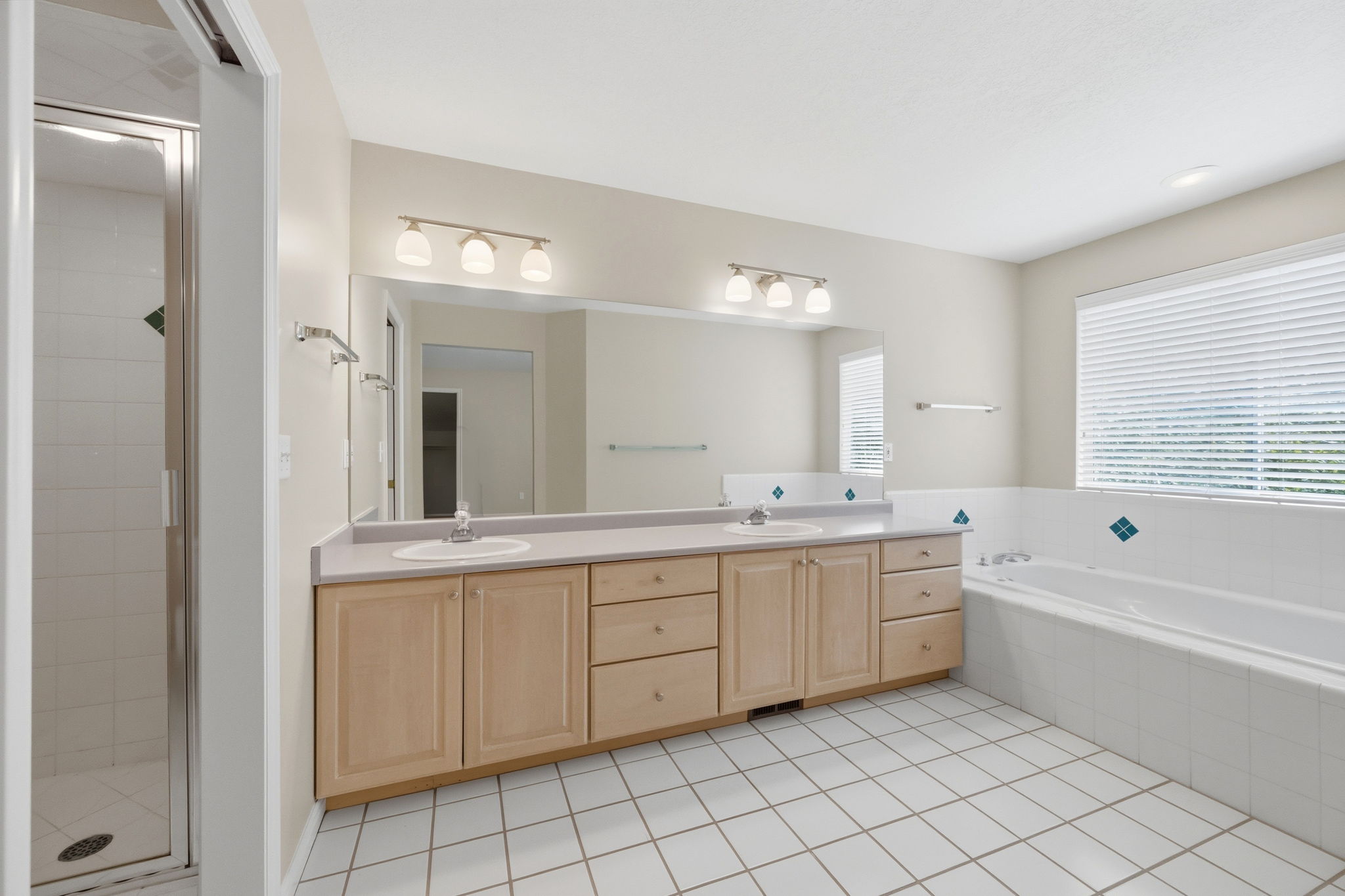 Bathroom featuring a double vanity with light wood cabinetry, a large built-in mirror, and a white tile floor