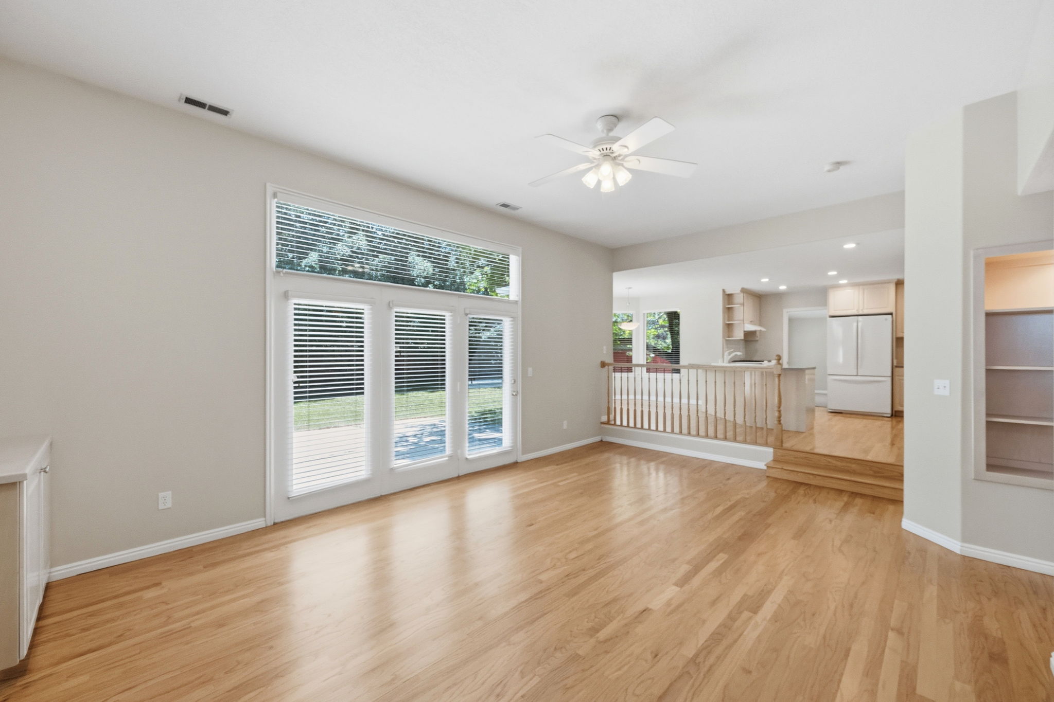 Spacious living area featuring wood-finish flooring, a ceiling fan, and a built-in cabinet