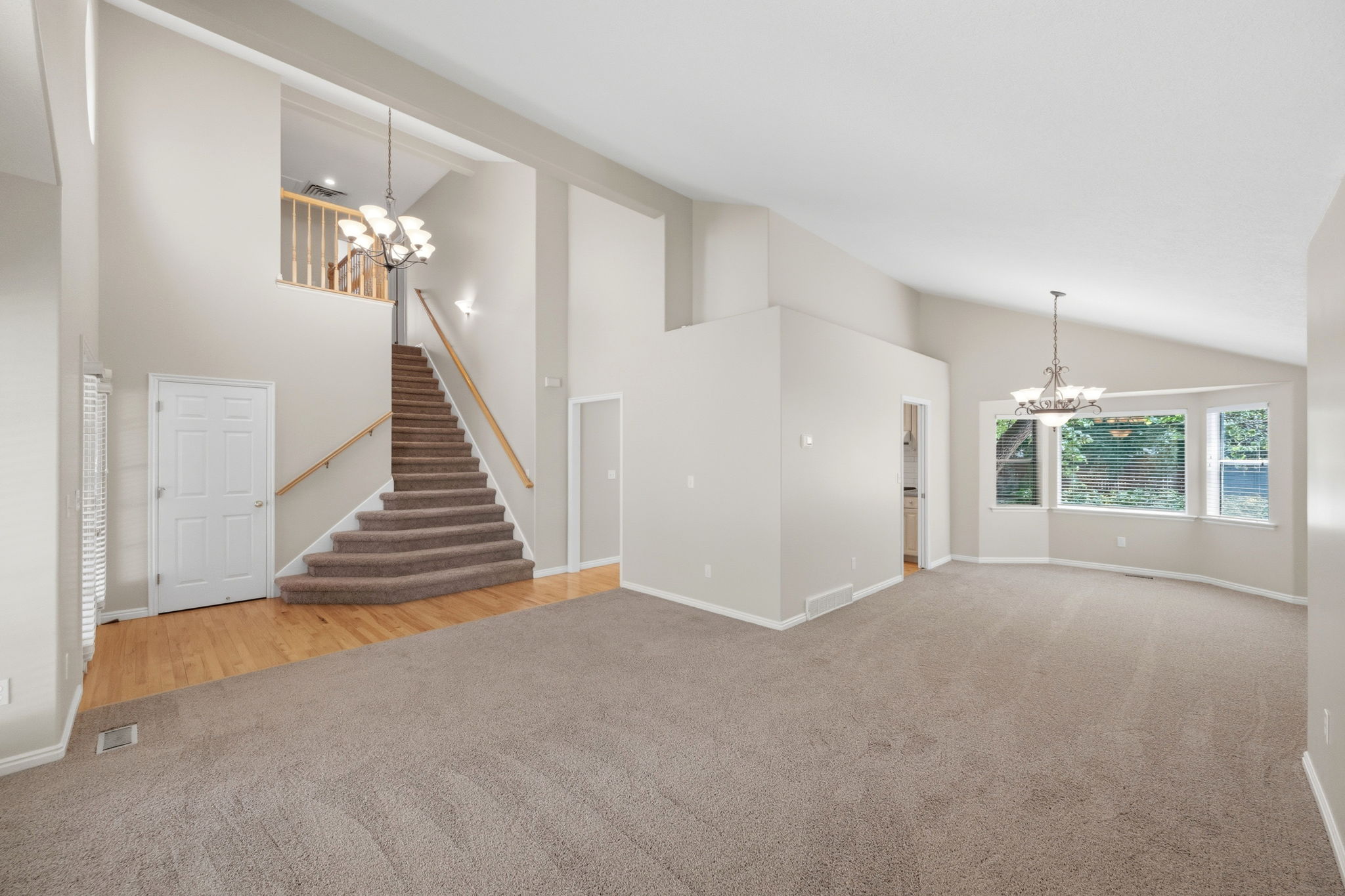 Spacious interior featuring a grand staircase with wood railing, vaulted ceilings, and a bay window