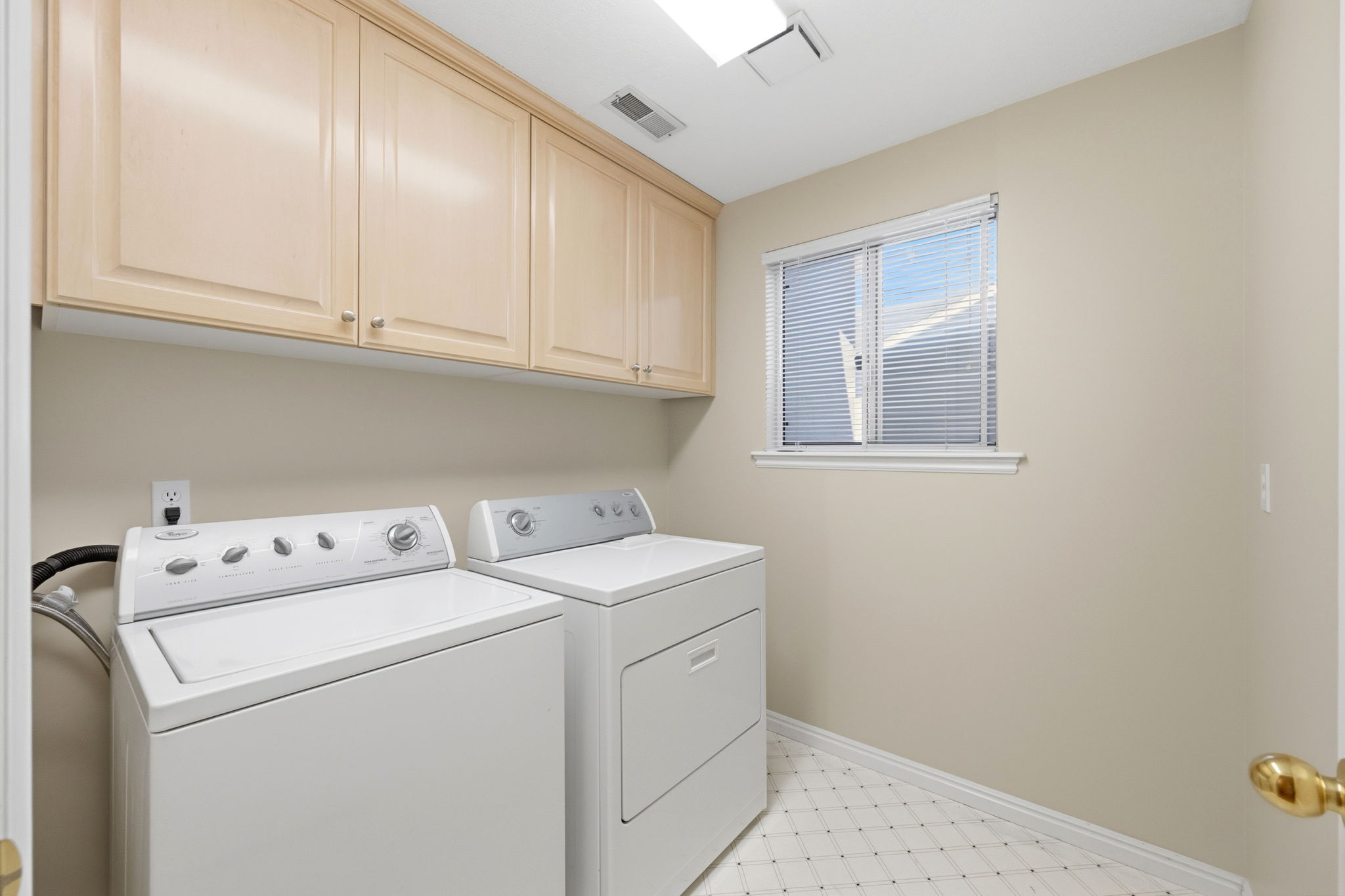 Laundry area featuring upper cabinetry, a window with blinds, and geometric pattern floor tiling