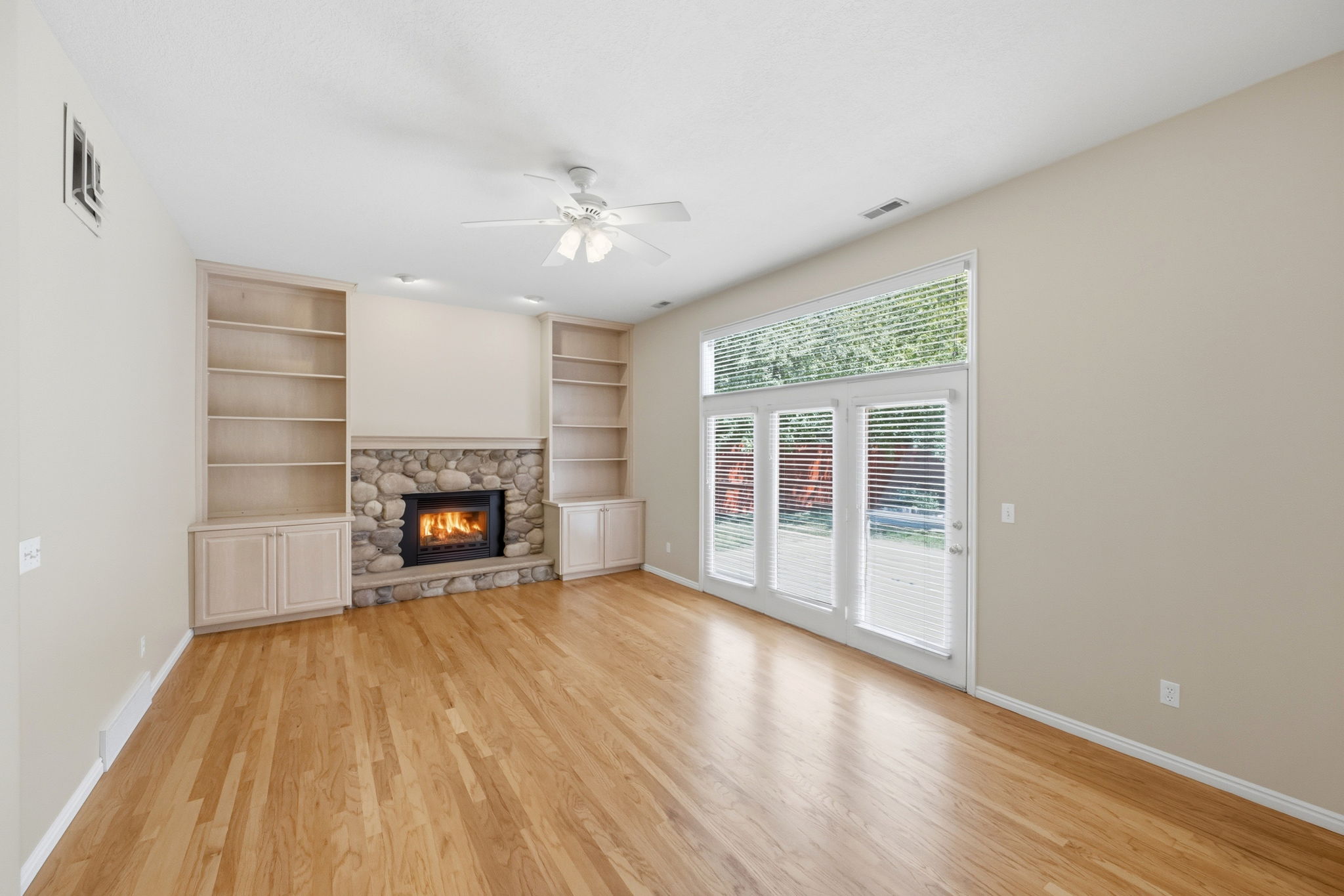 Living area featuring wood-finish flooring, a stone-surround fireplace with hearth, and built-in shelving with cabinetry