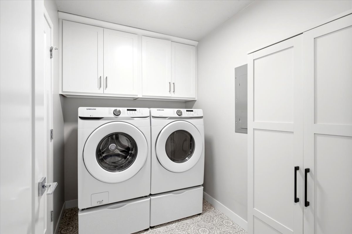 Dedicated laundry area featuring patterned tile flooring, overhead white cabinetry, and a full-height utility closet with matte black hardware