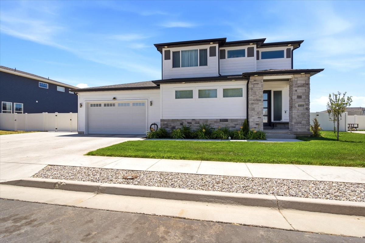 Contemporary exterior featuring white horizontal siding, stacked stone accents, a dark-framed entry door, a two-car garage with a panel door, and a concrete driveway