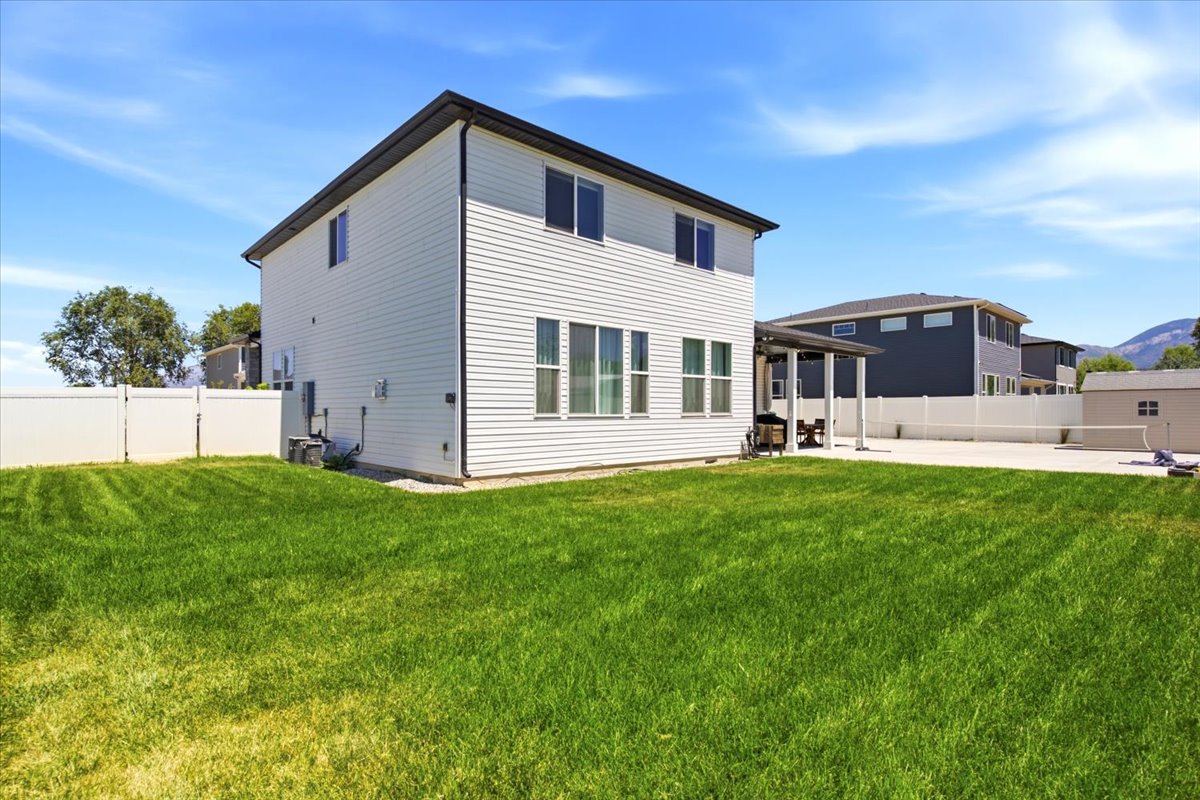 Expansive backyard featuring a green lawn, a white privacy fence, a concrete patio, and a covered patio area