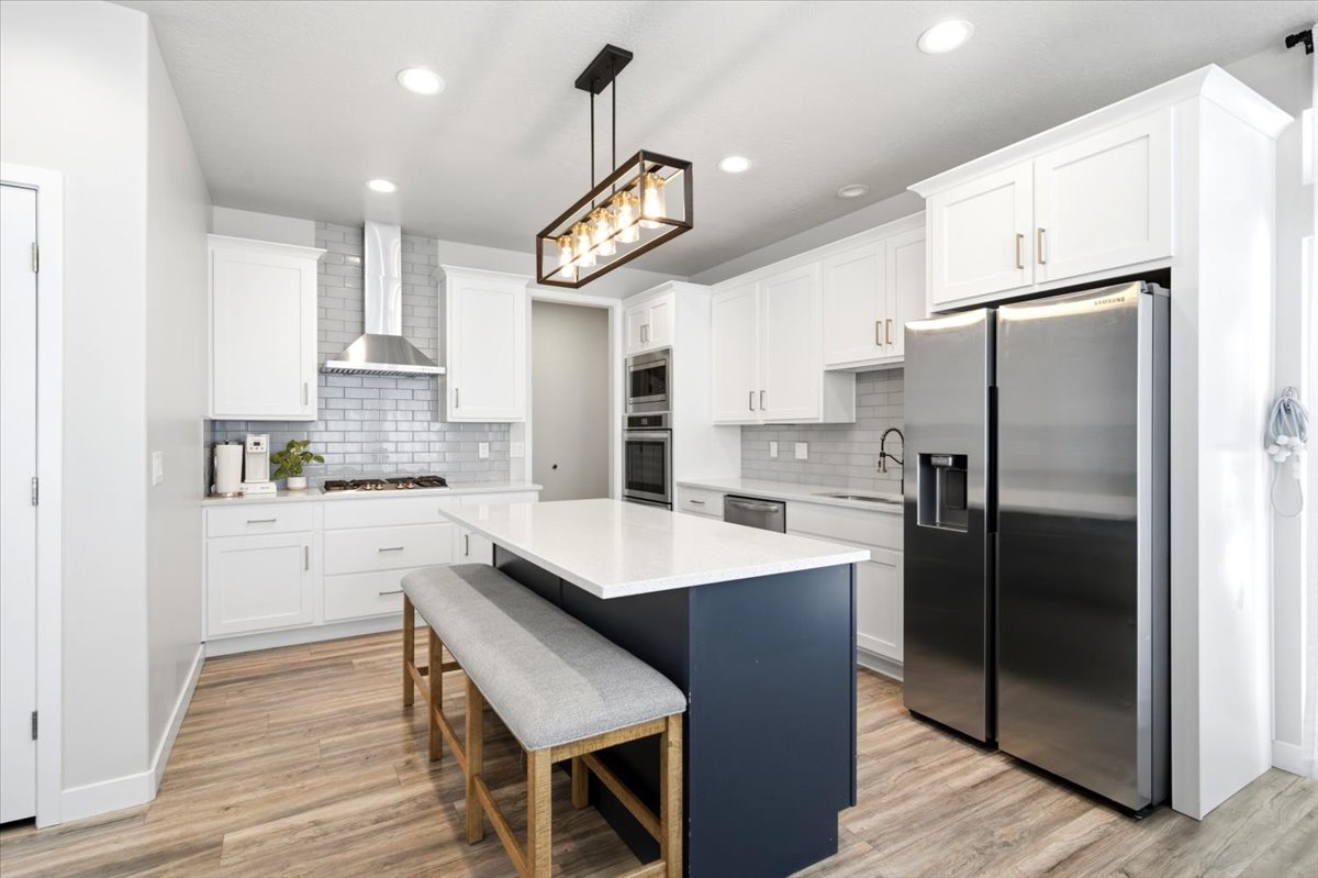 Bright kitchen featuring a white subway tile backsplash, stainless steel appliances, a center island with a quartz countertop, white shaker cabinetry, and wood-finish flooring