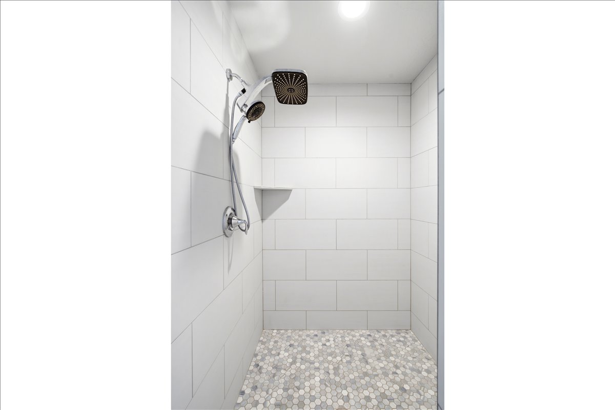 Shower stall featuring white subway tile, a rain showerhead, a handheld sprayer, a built-in shelf, and hexagonal mosaic floor tiling