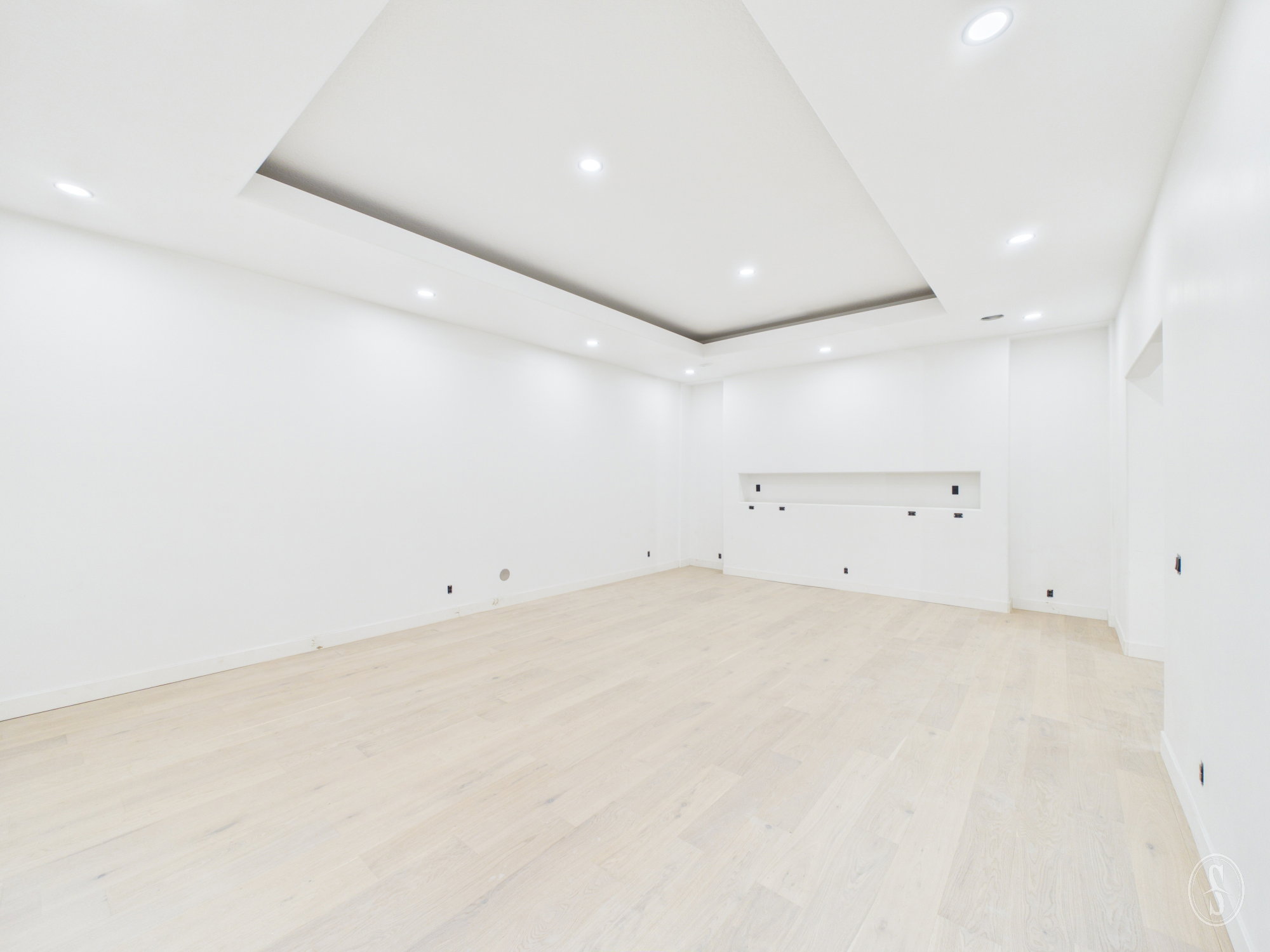 Spacious room featuring light wood-finish flooring, recessed lighting, and a tray ceiling design
