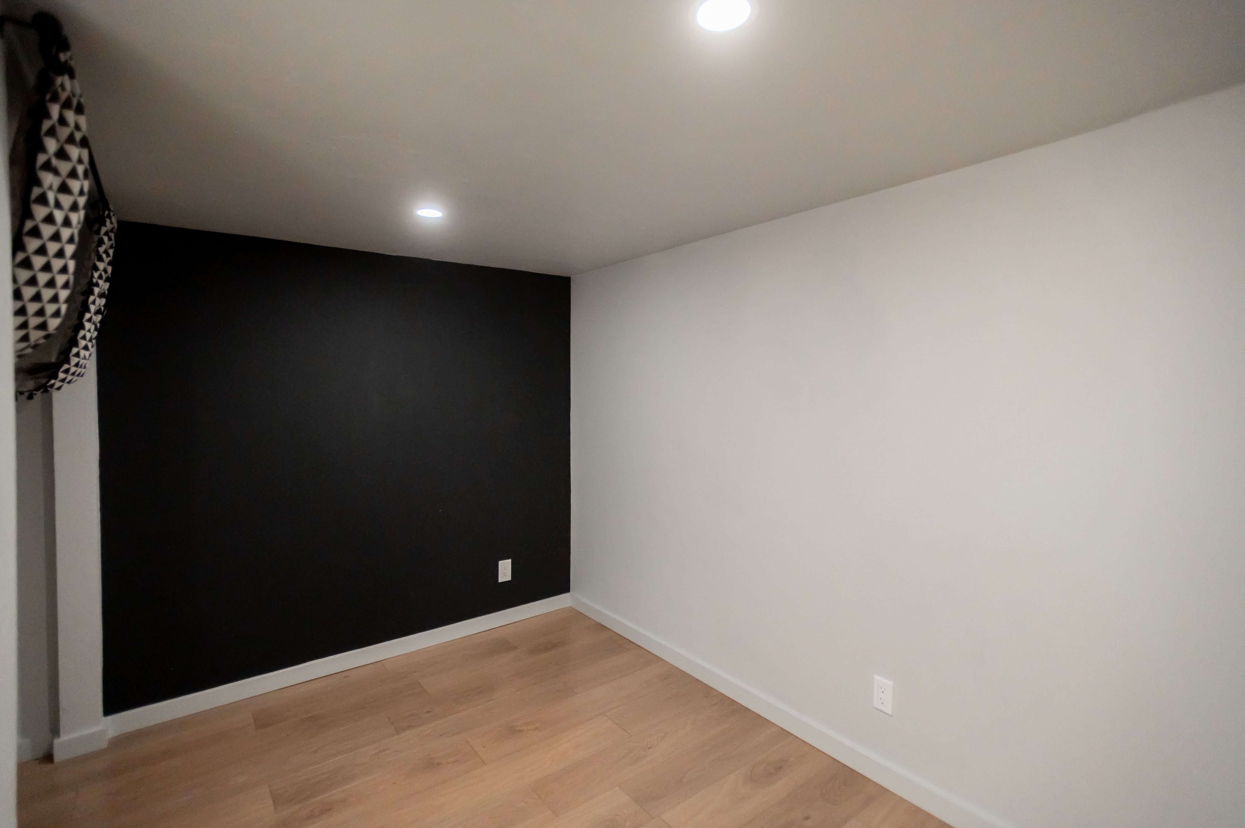 Interior room featuring a contrasting black accent wall, light wood-finish flooring, white baseboards, and recessed ceiling lighting