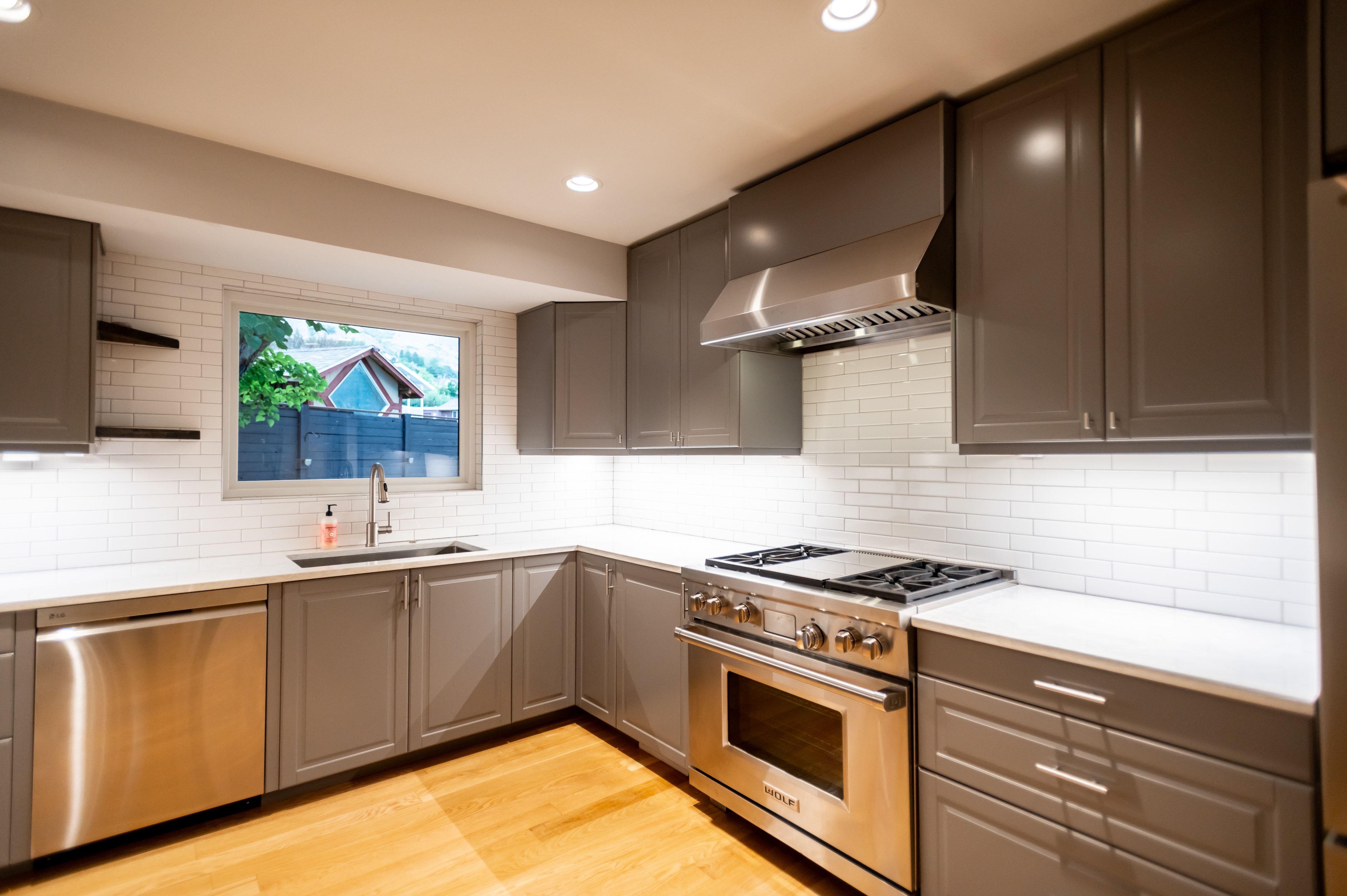 Contemporary kitchen featuring gray cabinetry, stainless steel appliances, white subway tile backsplash, recessed lighting, and wood-finish flooring