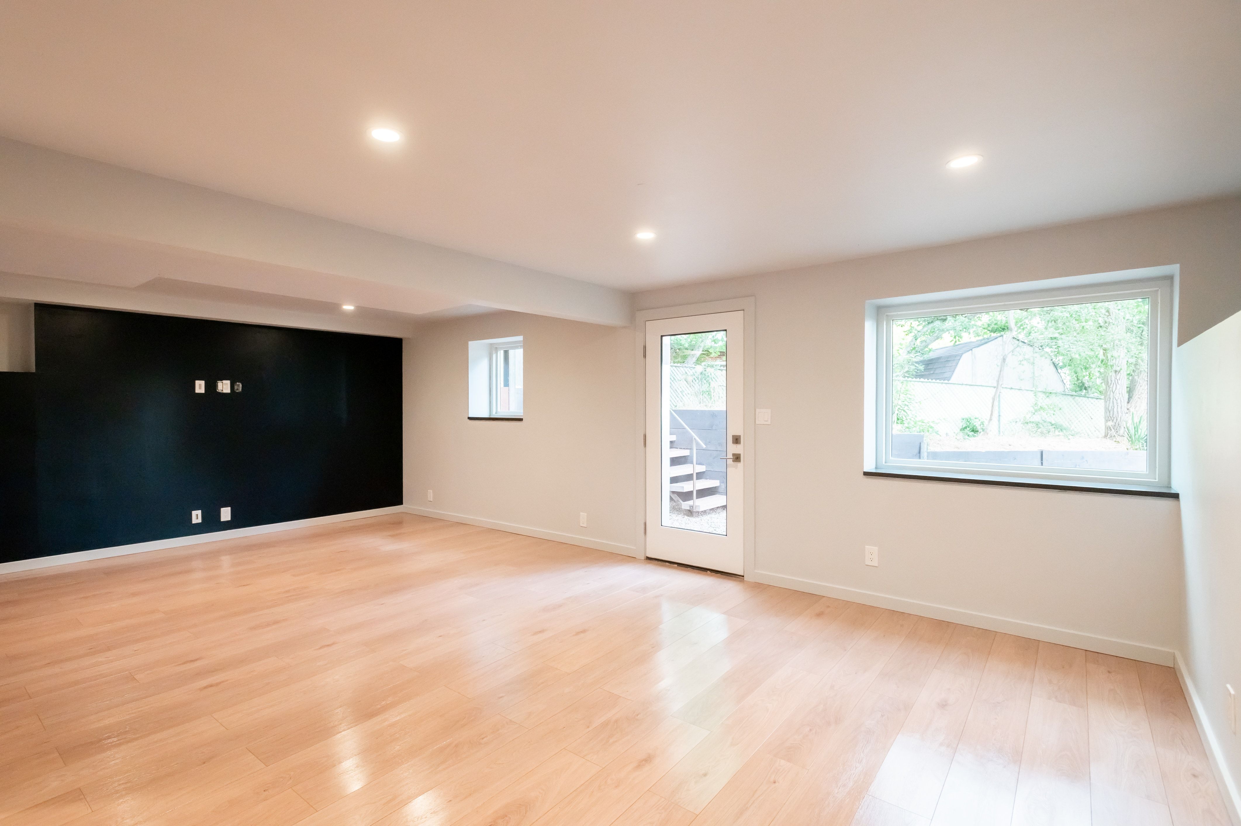 Spacious room featuring light wood-finish flooring, recessed lighting, and a dark accent wall