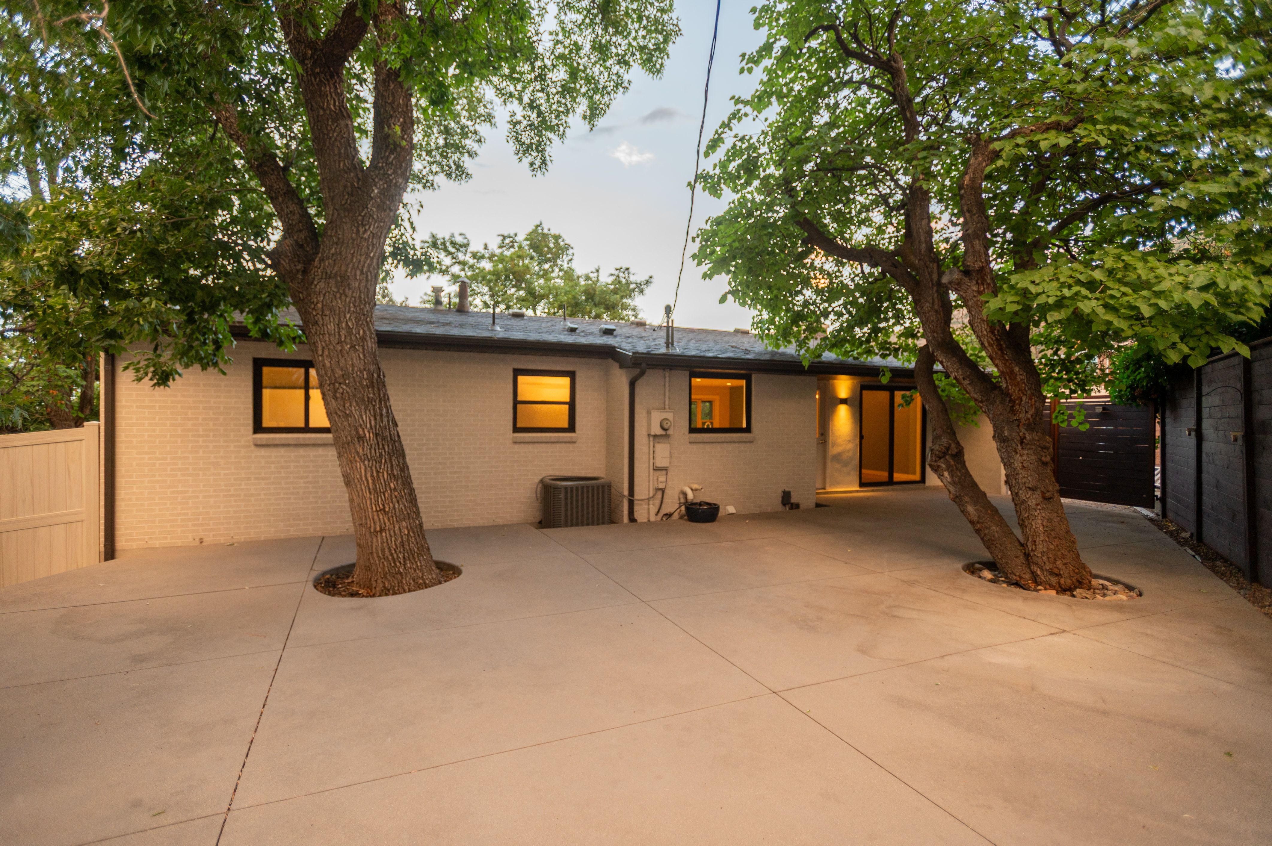 Expansive concrete patio area with mature trees and a white brick exterior