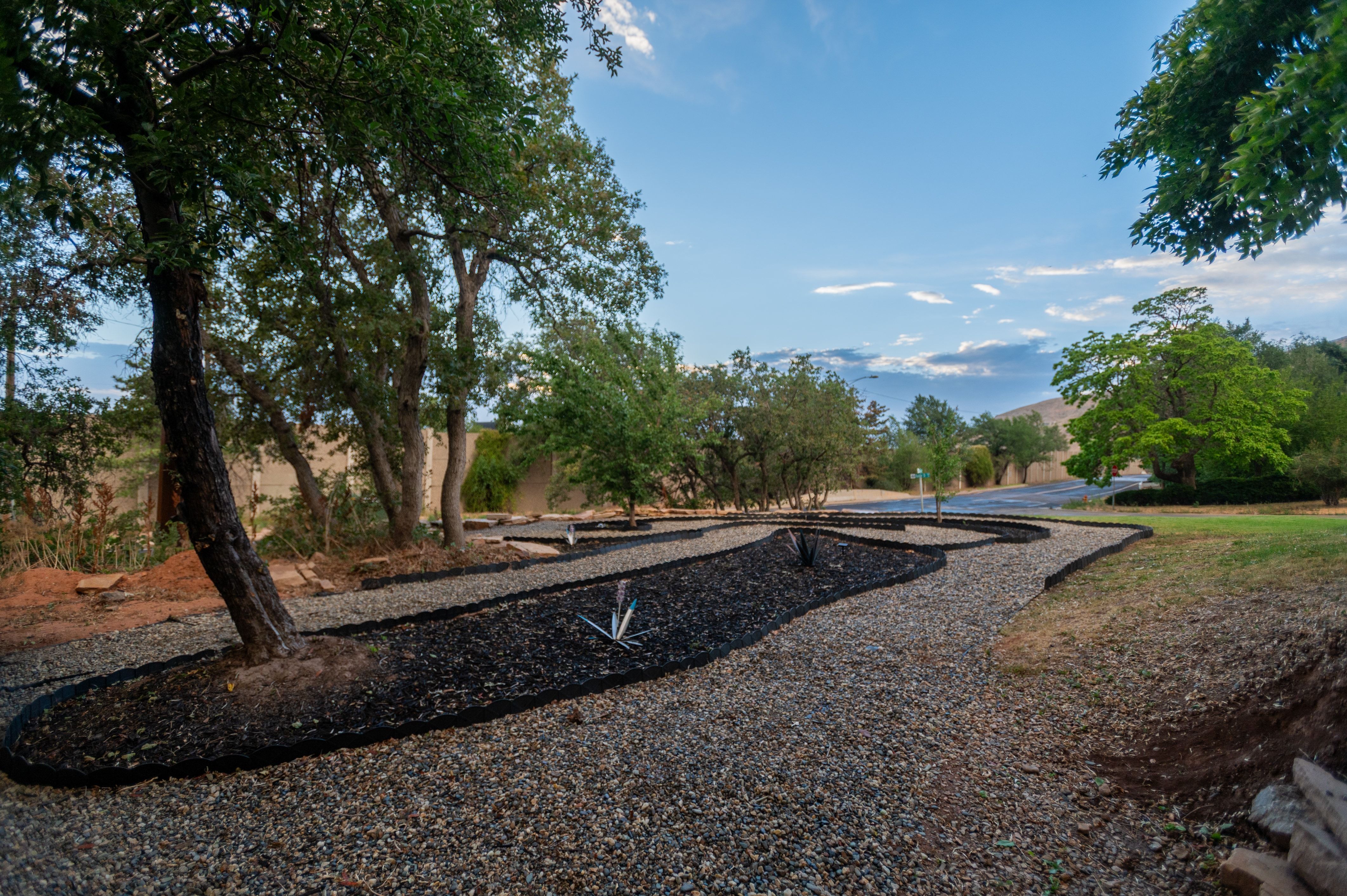 Landscaped exterior featuring a gravel pathway, defined planting beds with dark mulch, and mature trees