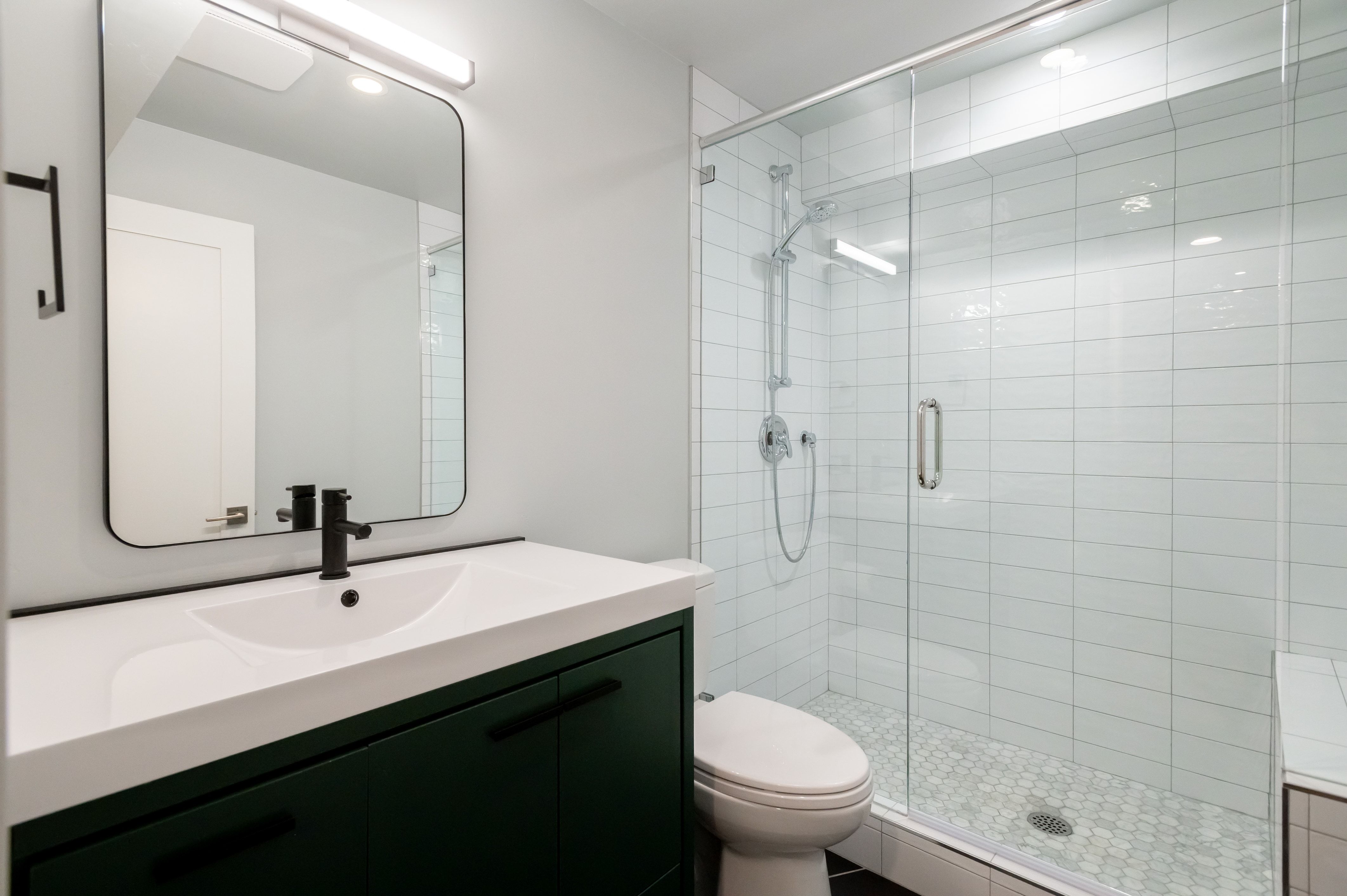 Modern bathroom featuring a dark green vanity with an integrated white sink, matte black faucet, and a large frameless mirror