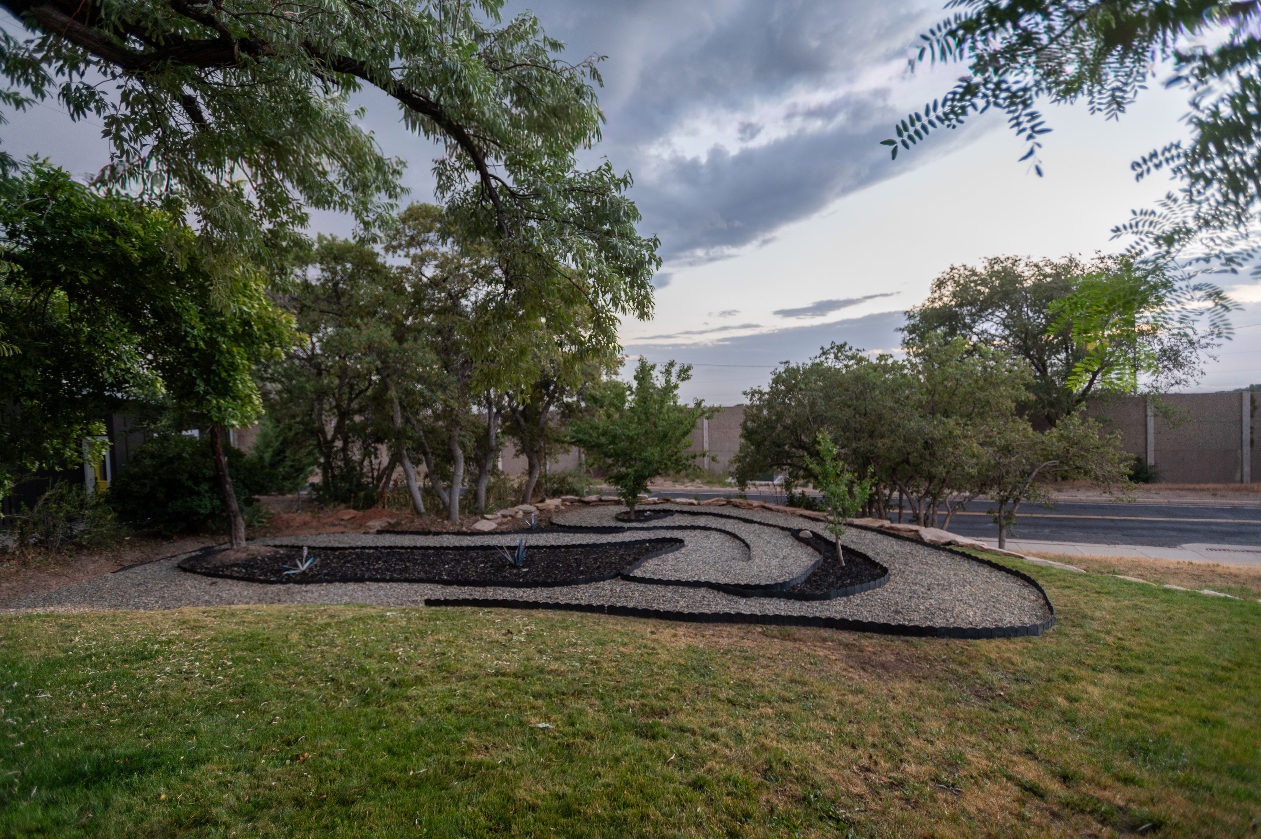 Landscaped front yard featuring a grass lawn, mature trees, and a decorative gravel and mulch bed