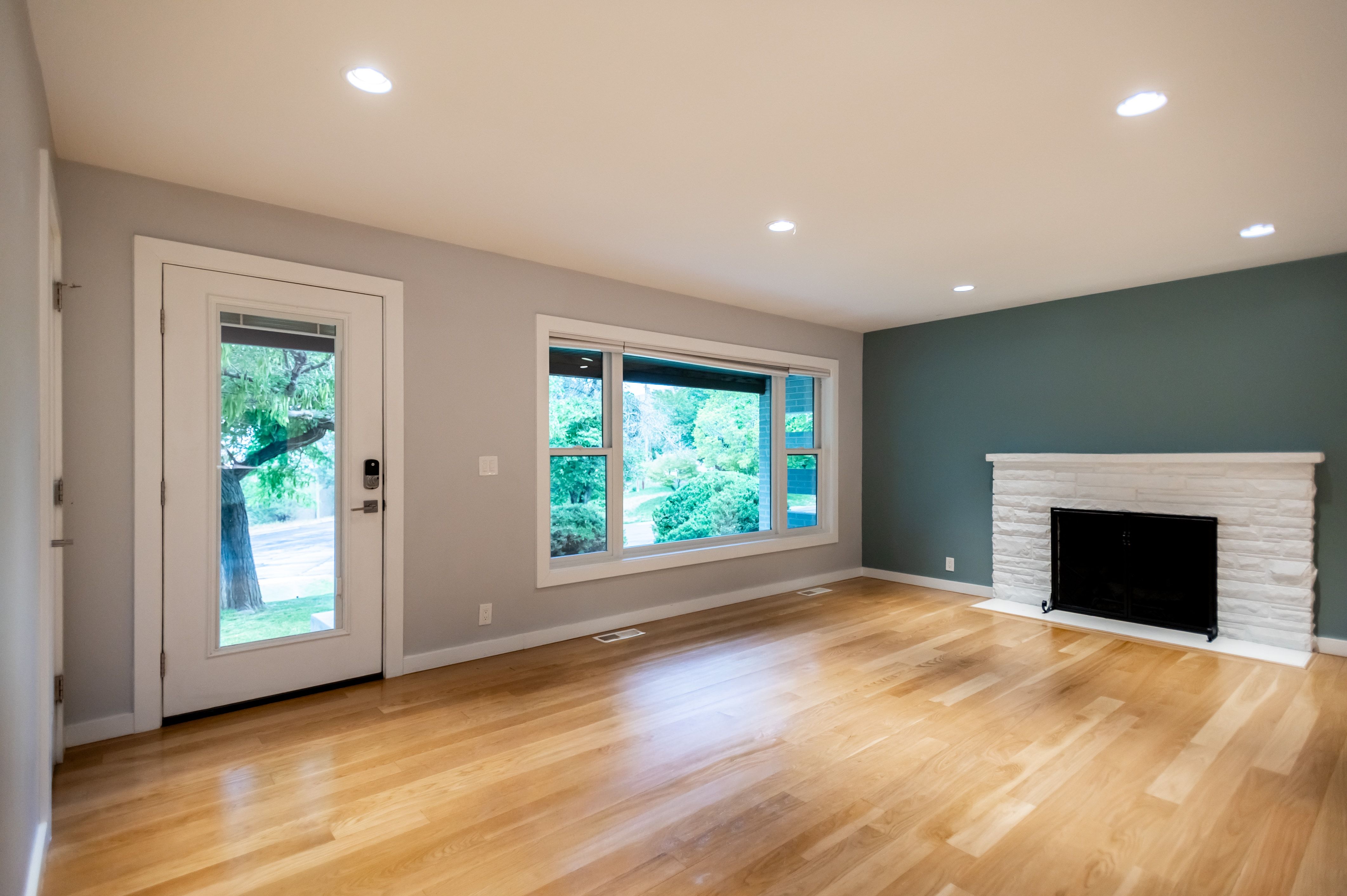 Open-concept living space featuring wood-finish flooring, recessed lighting, and a white stone-clad fireplace
