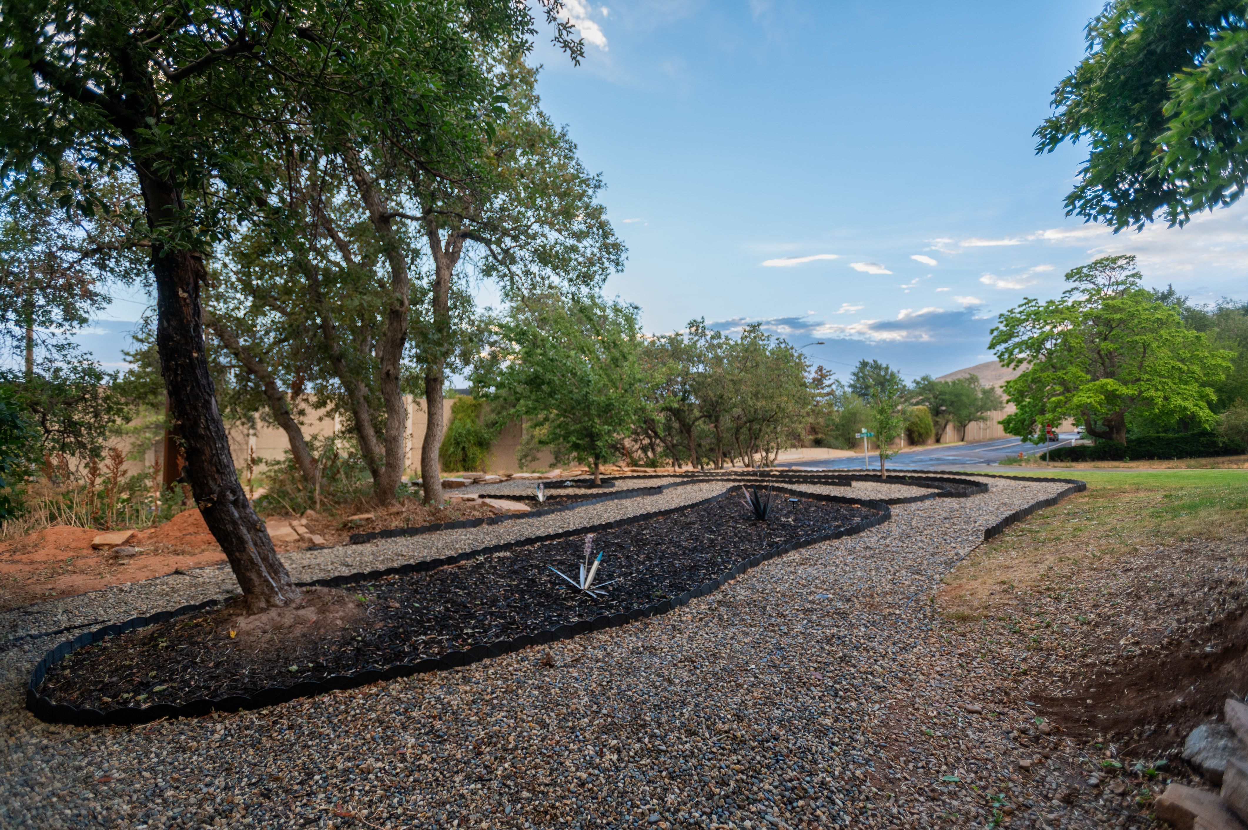 Landscaped exterior featuring a gravel pathway, dark mulch beds, mature trees, and a grassy area