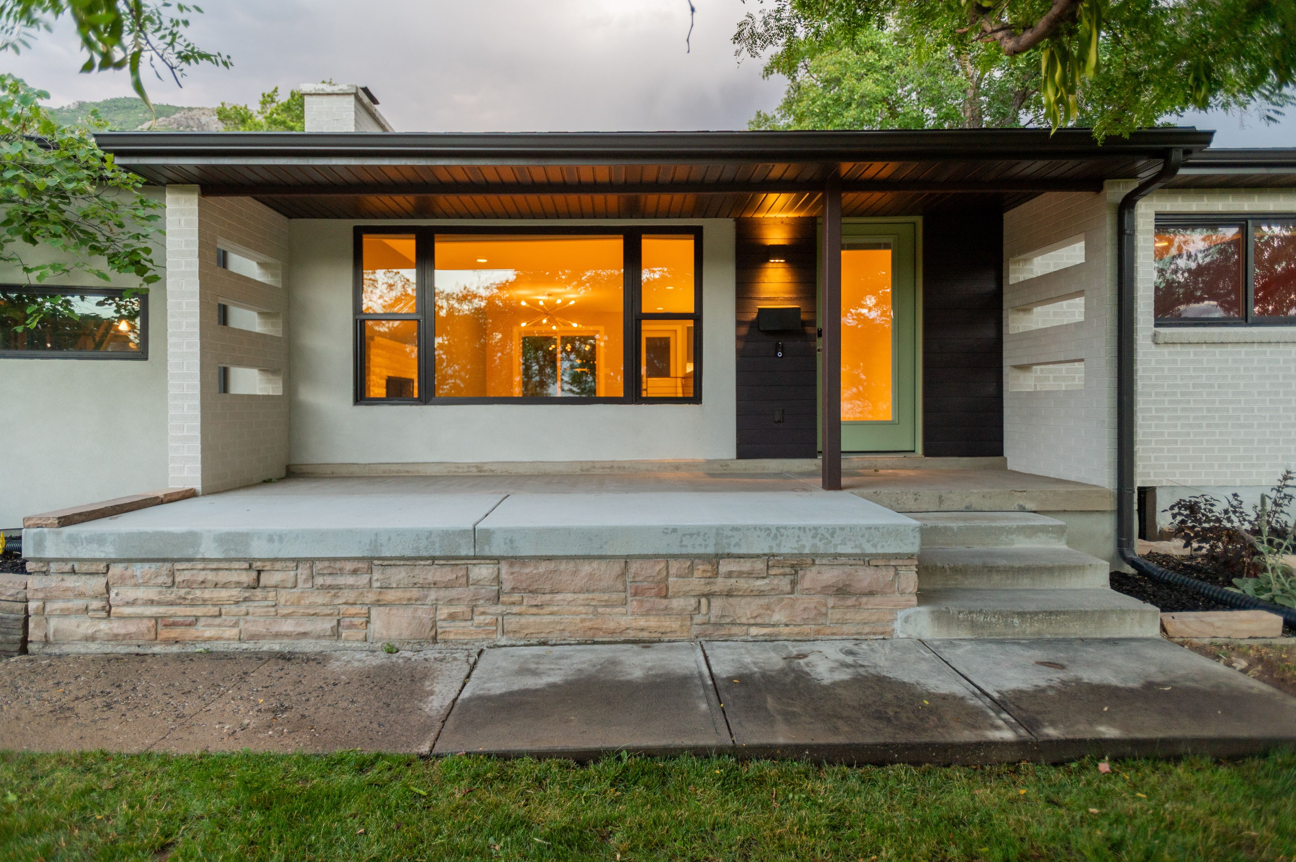 Mid-century modern exterior featuring a covered entry, painted brick accents, stacked stone detailing, a prominent picture window, and a light green entry door