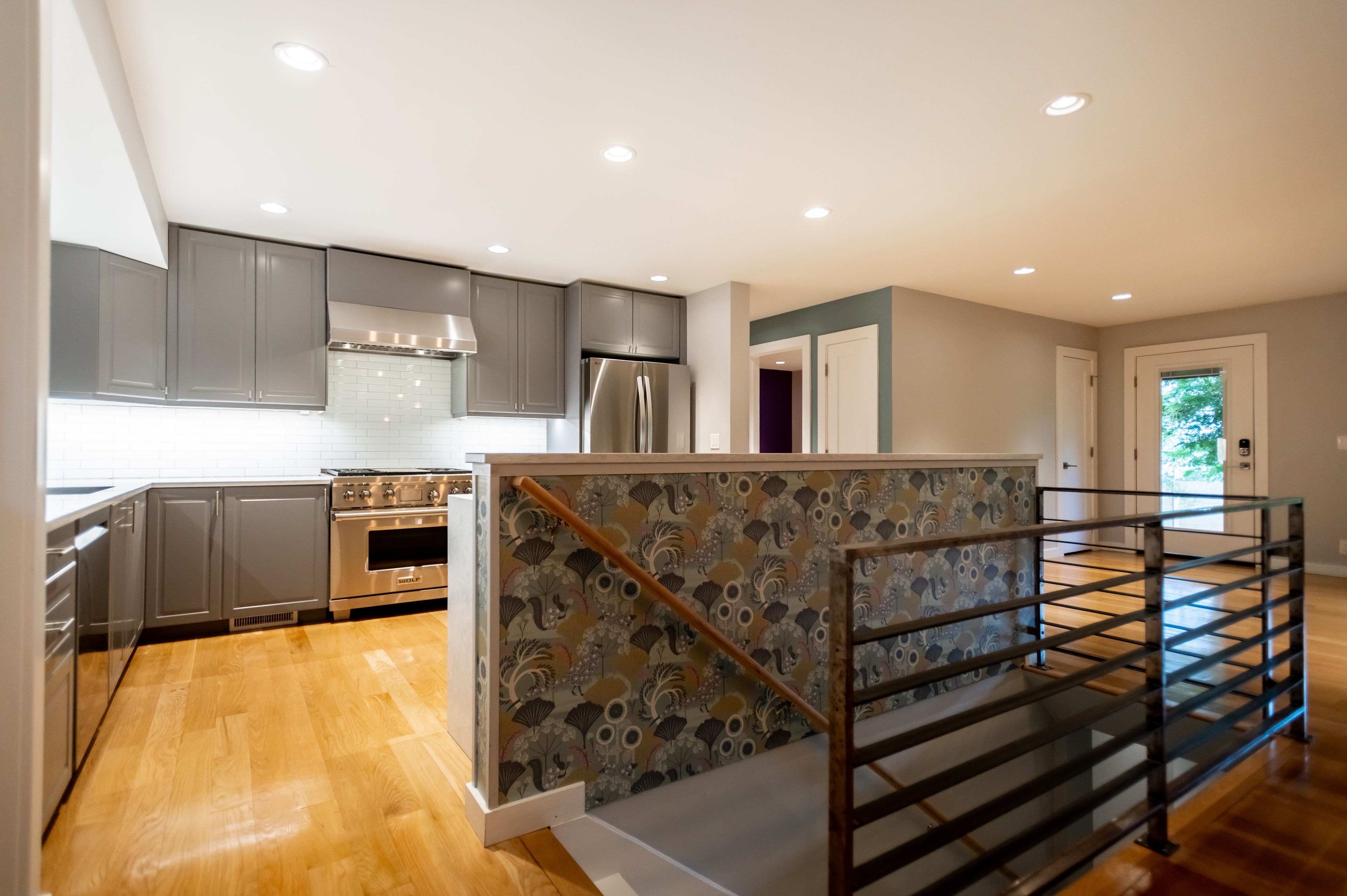 Modern kitchen featuring sleek gray cabinetry, stainless steel appliances, a white subway tile backsplash, and light wood-finish flooring