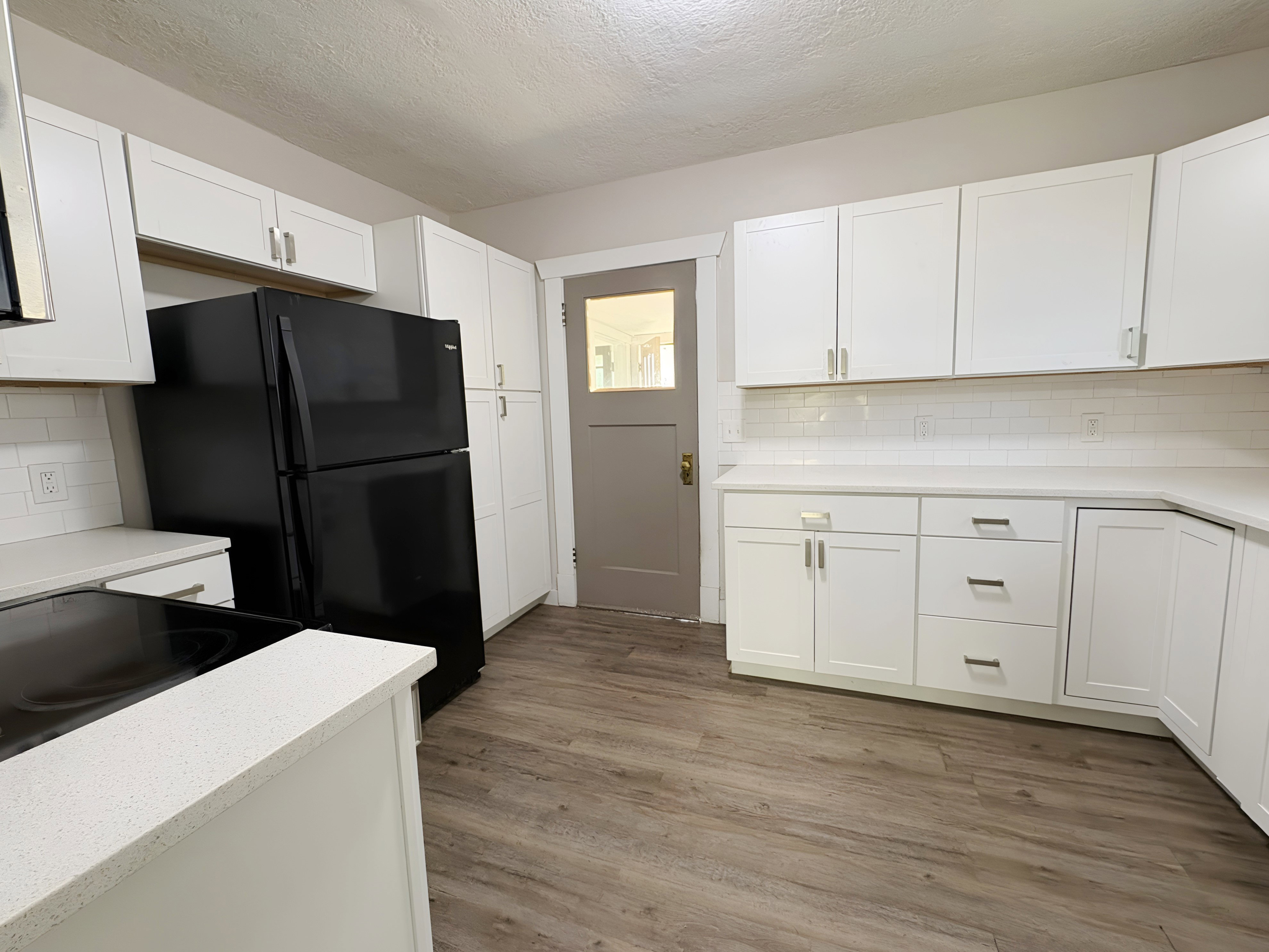 Kitchen featuring white shaker cabinetry, light-toned countertops, white subway tile backsplash, black refrigerator, and wood-finish flooring