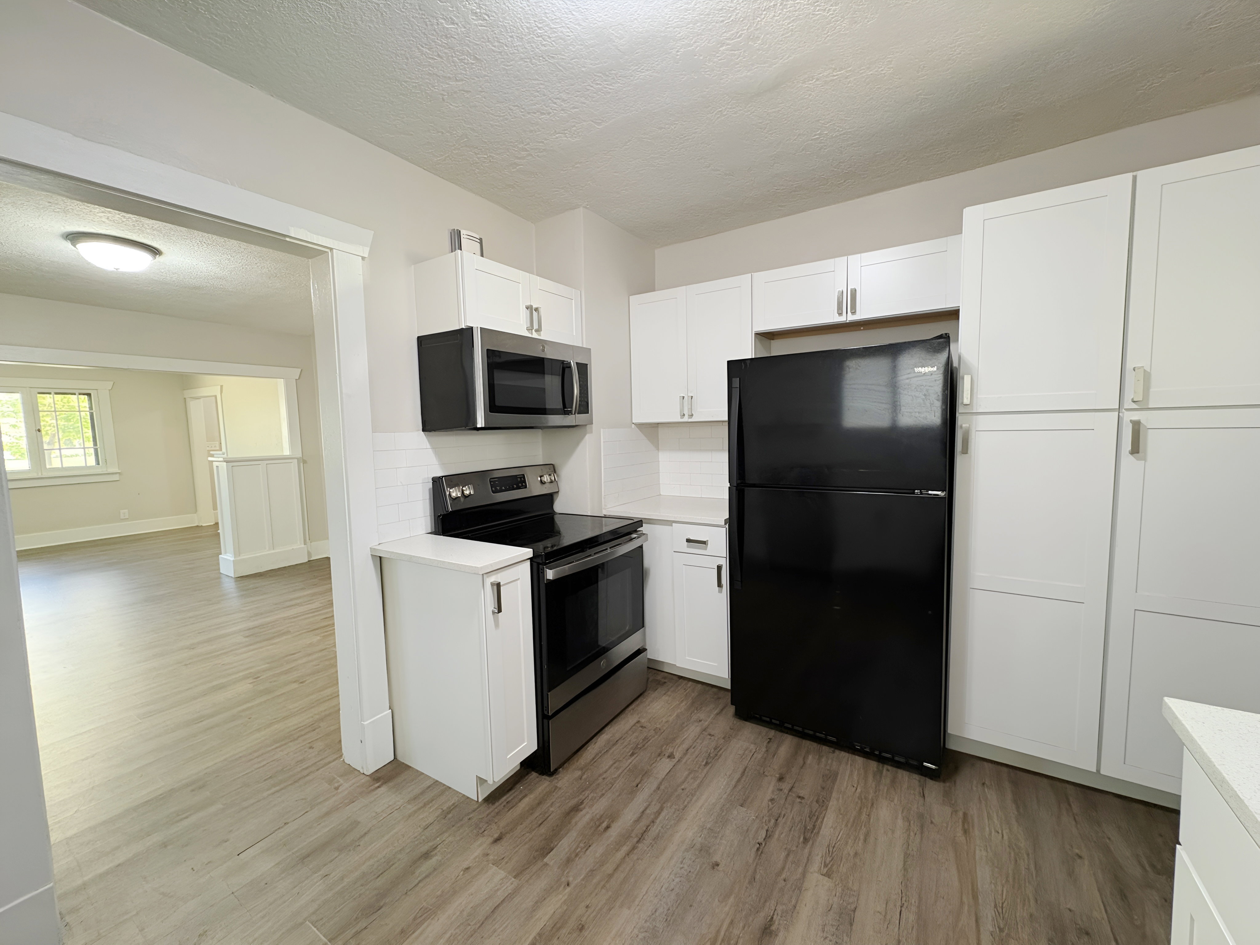 Kitchen featuring white shaker-style cabinetry, stainless steel appliances, a white subway tile backsplash, light-toned countertops, and wood-finish flooring