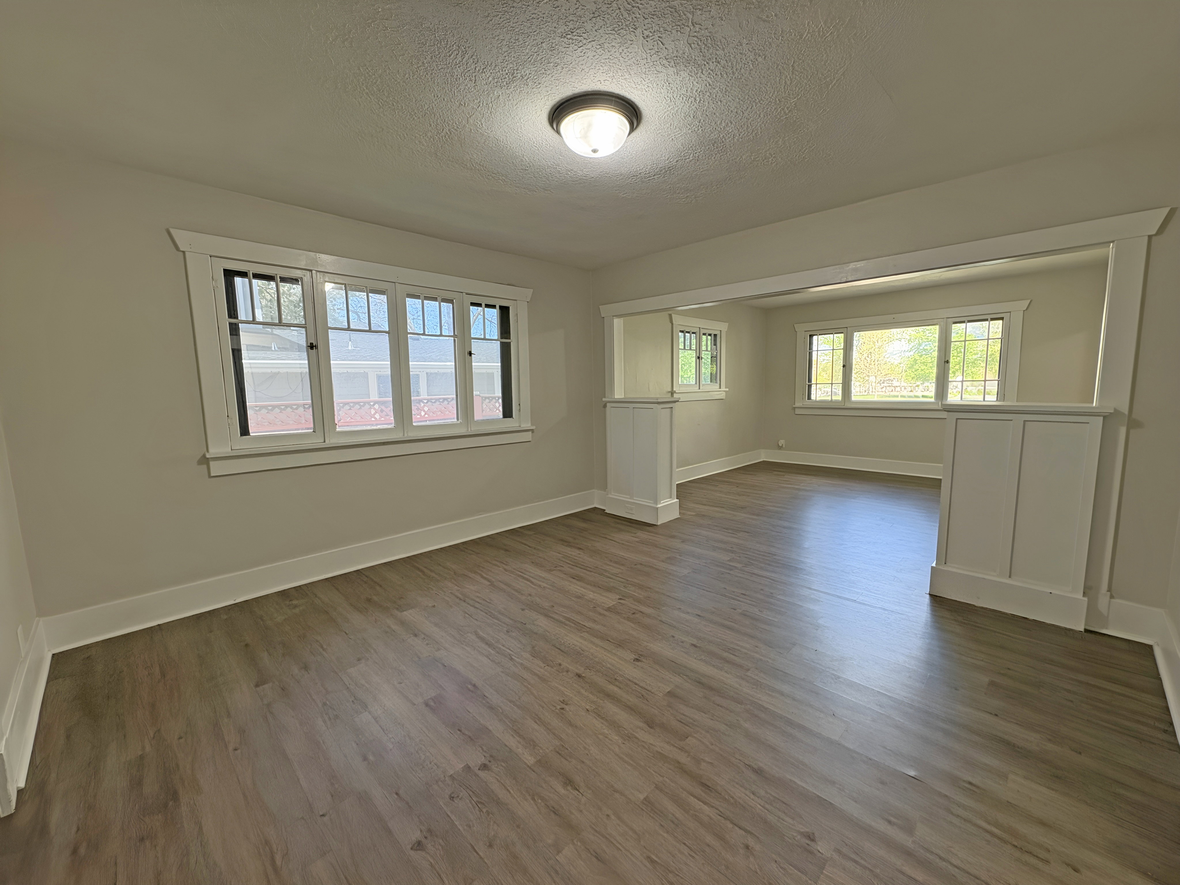 Spacious interior featuring wood-finish flooring, a contemporary ceiling light fixture, and white baseboards