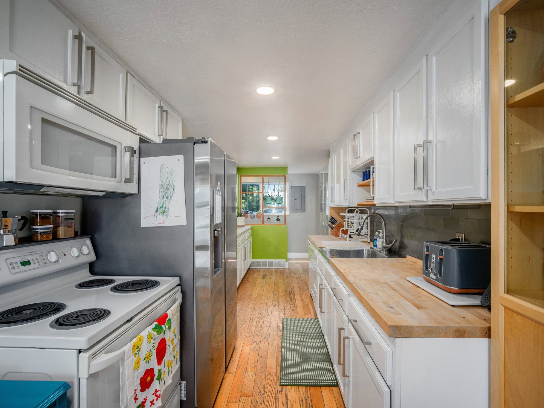 Galley kitchen featuring wood-finish flooring, white cabinetry, stainless steel refrigerator, white range with microwave above, and natural wood countertops