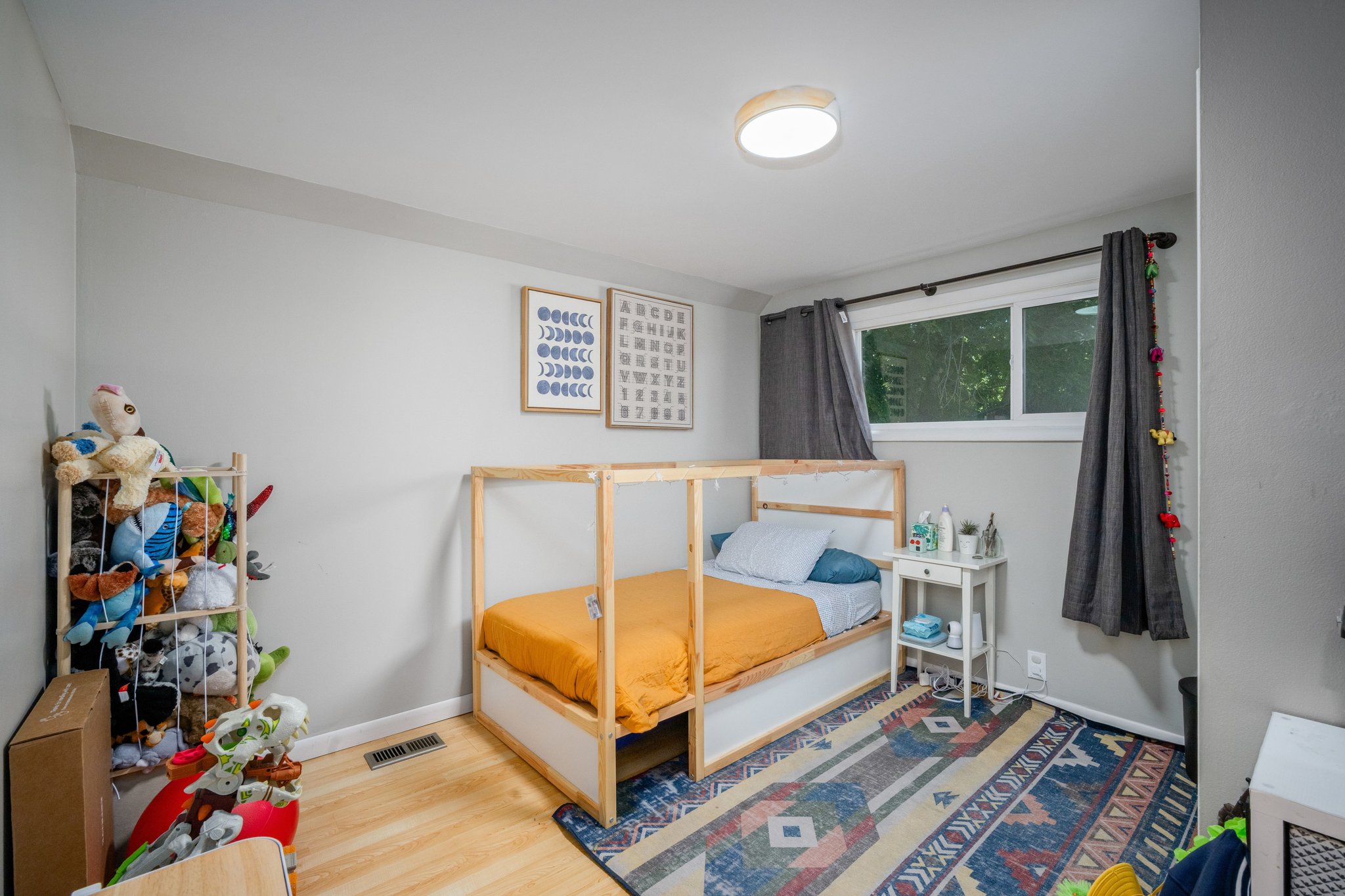 Bright room featuring light wood-finish flooring, a contemporary ceiling light fixture, a window with dark curtain rods, and light gray wall paint