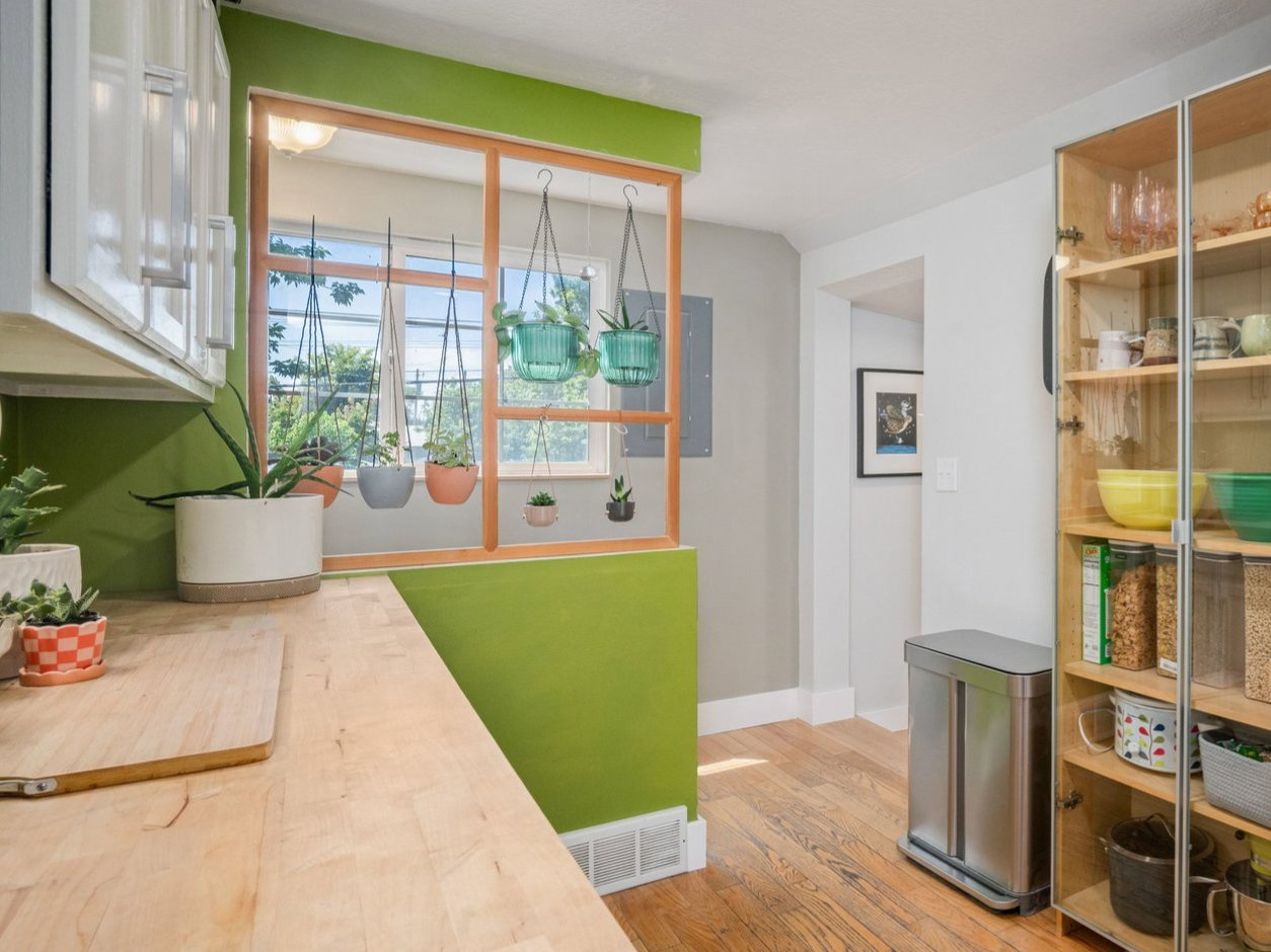 Bright kitchen featuring wood-finish flooring, white cabinetry, butcher block countertops, a built-in dishwasher, and a glass-front display cabinet
