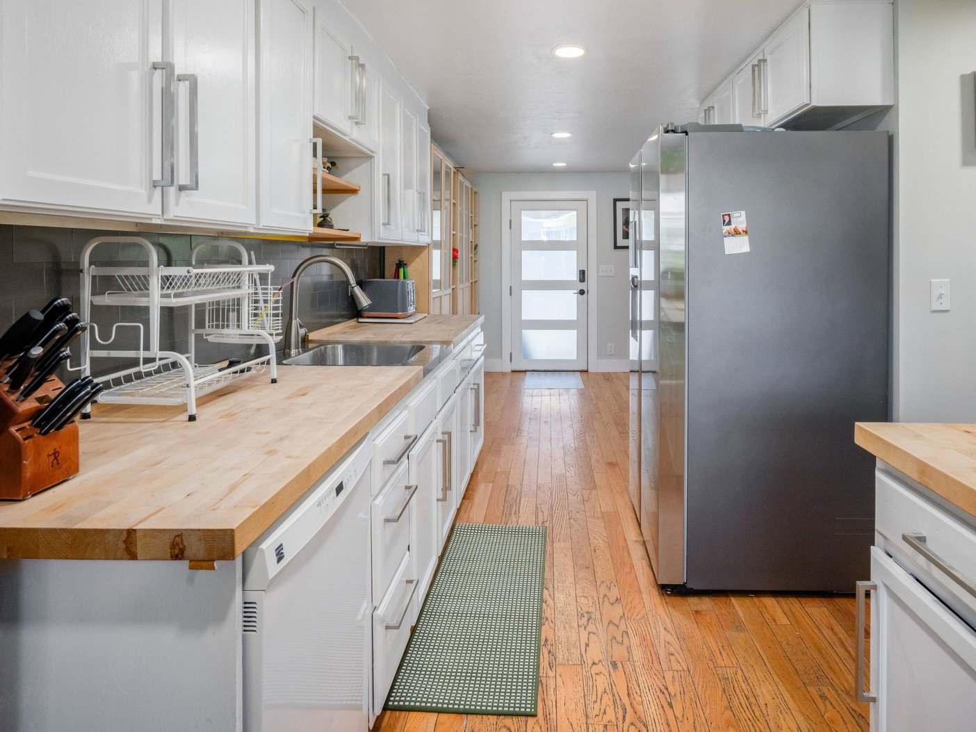 Kitchen featuring white cabinetry, wood-finish countertops, stainless steel sink, and wood-finish flooring