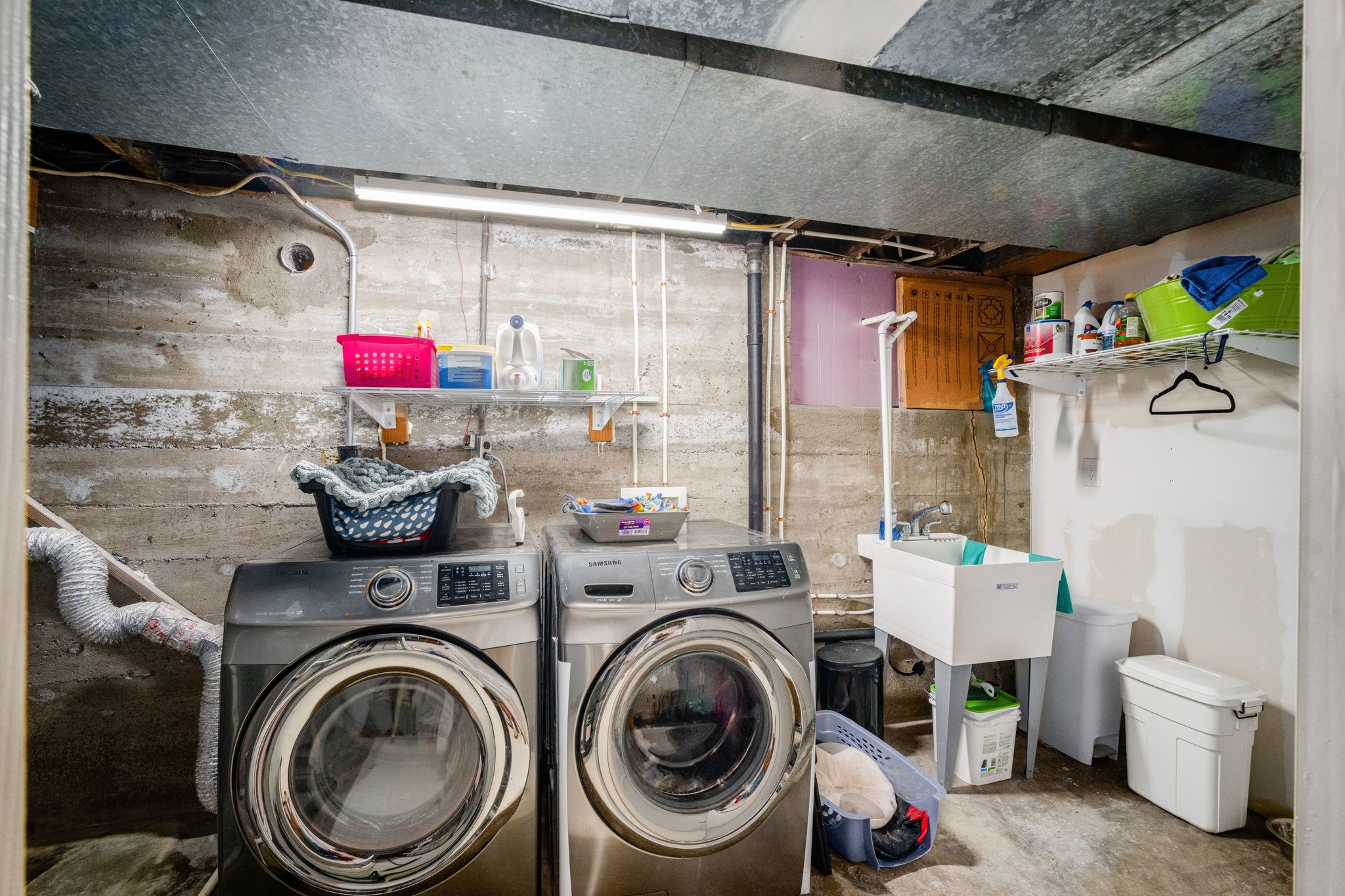Laundry area featuring a utility sink, wall-mounted shelving, and concrete walls