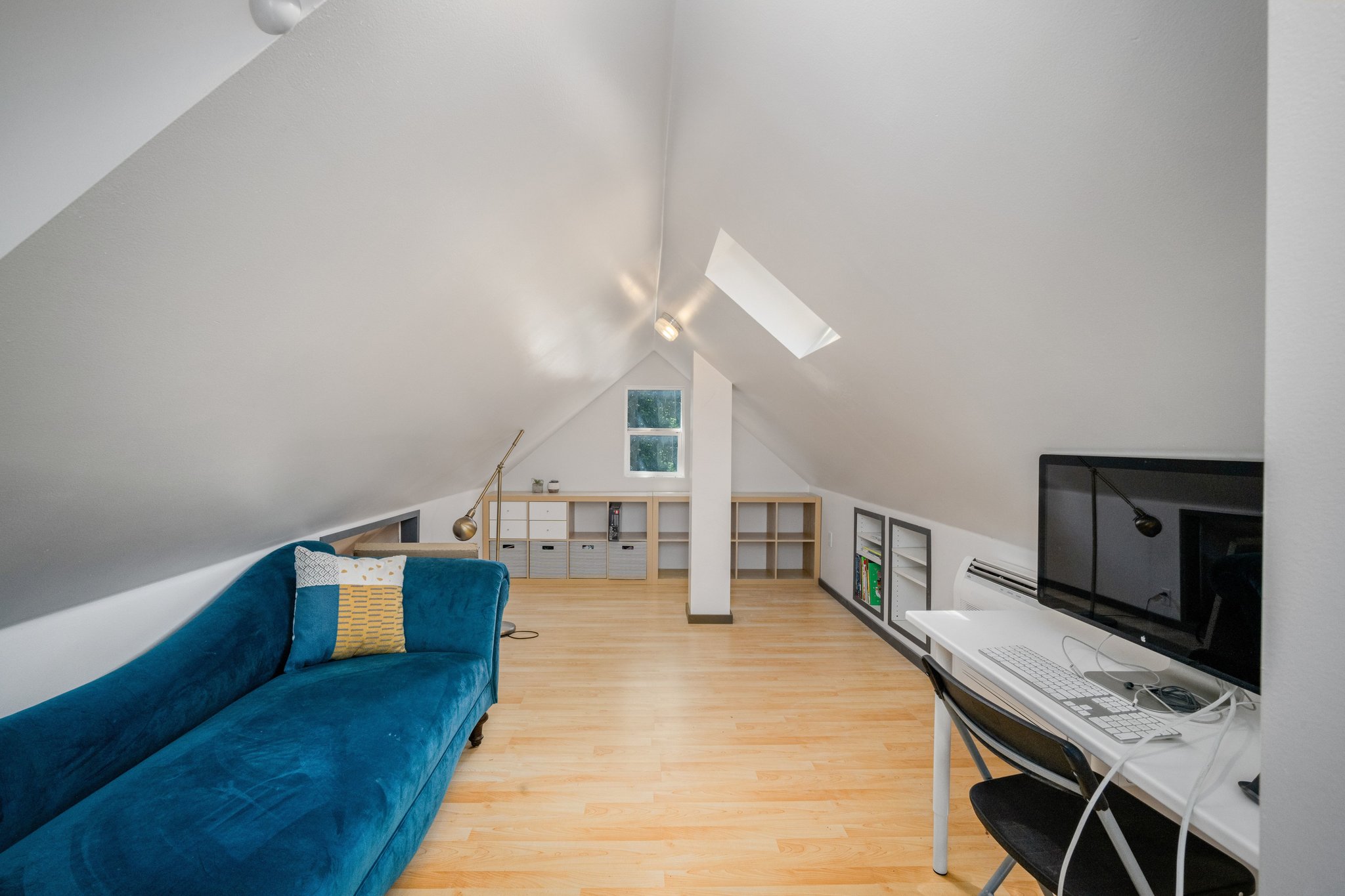 Attic room featuring bright white walls, skylight, wood-finish flooring, and built-in shelving