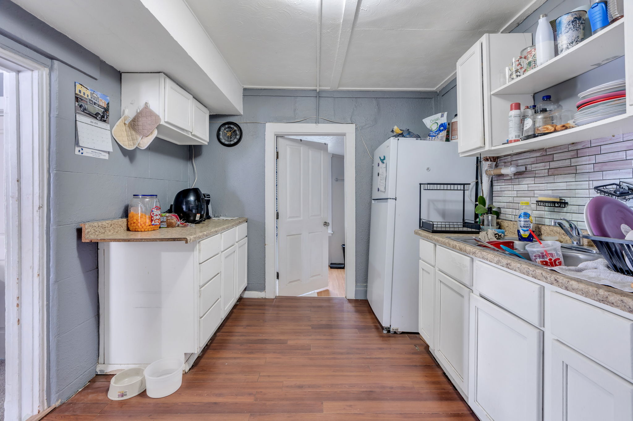 Kitchen featuring wood-finish flooring, white cabinetry, granite-look countertops, and a white tile backsplash