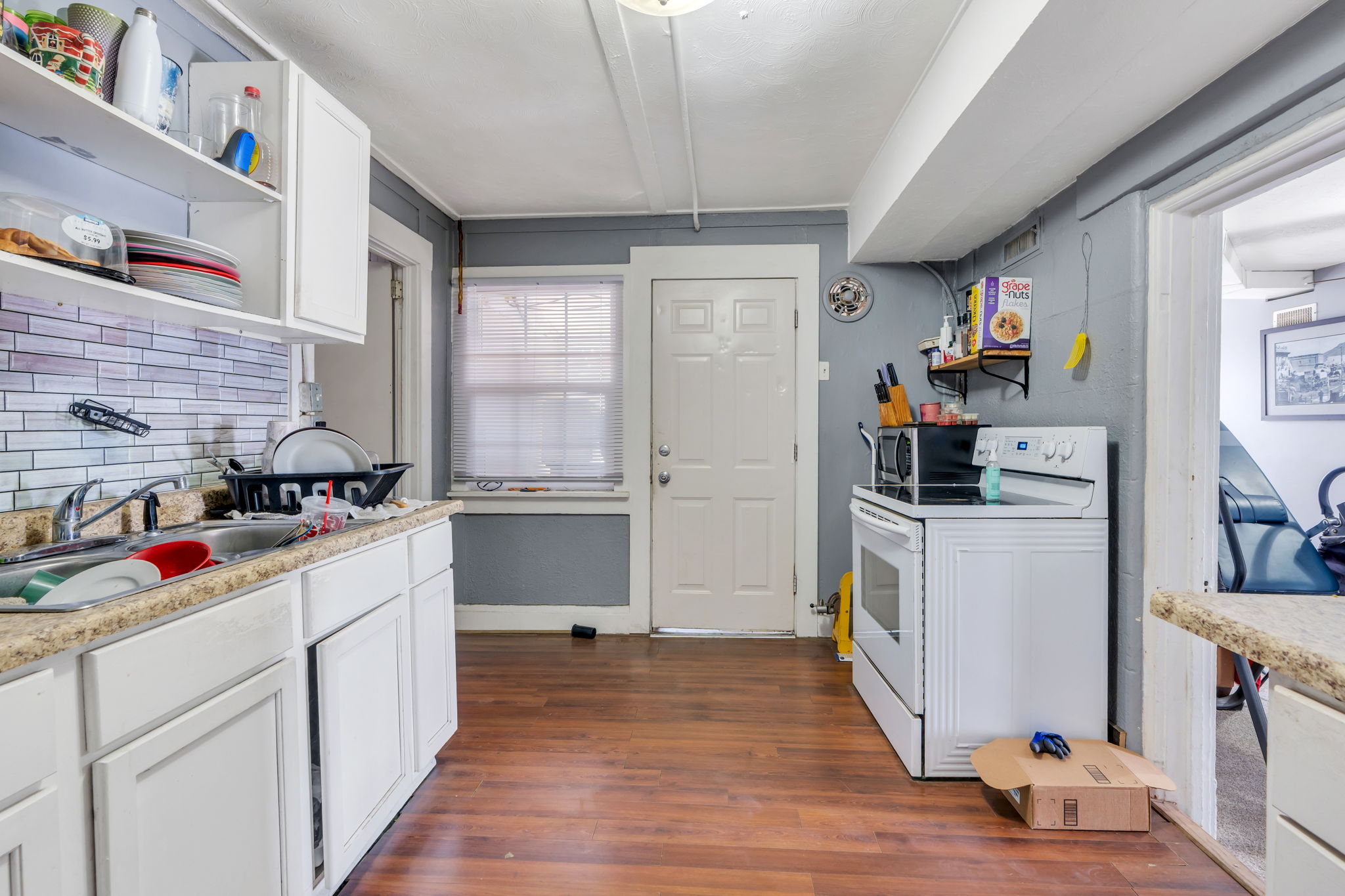 Kitchen featuring wood-finish flooring, white cabinetry, a tiled backsplash, and a window for natural light