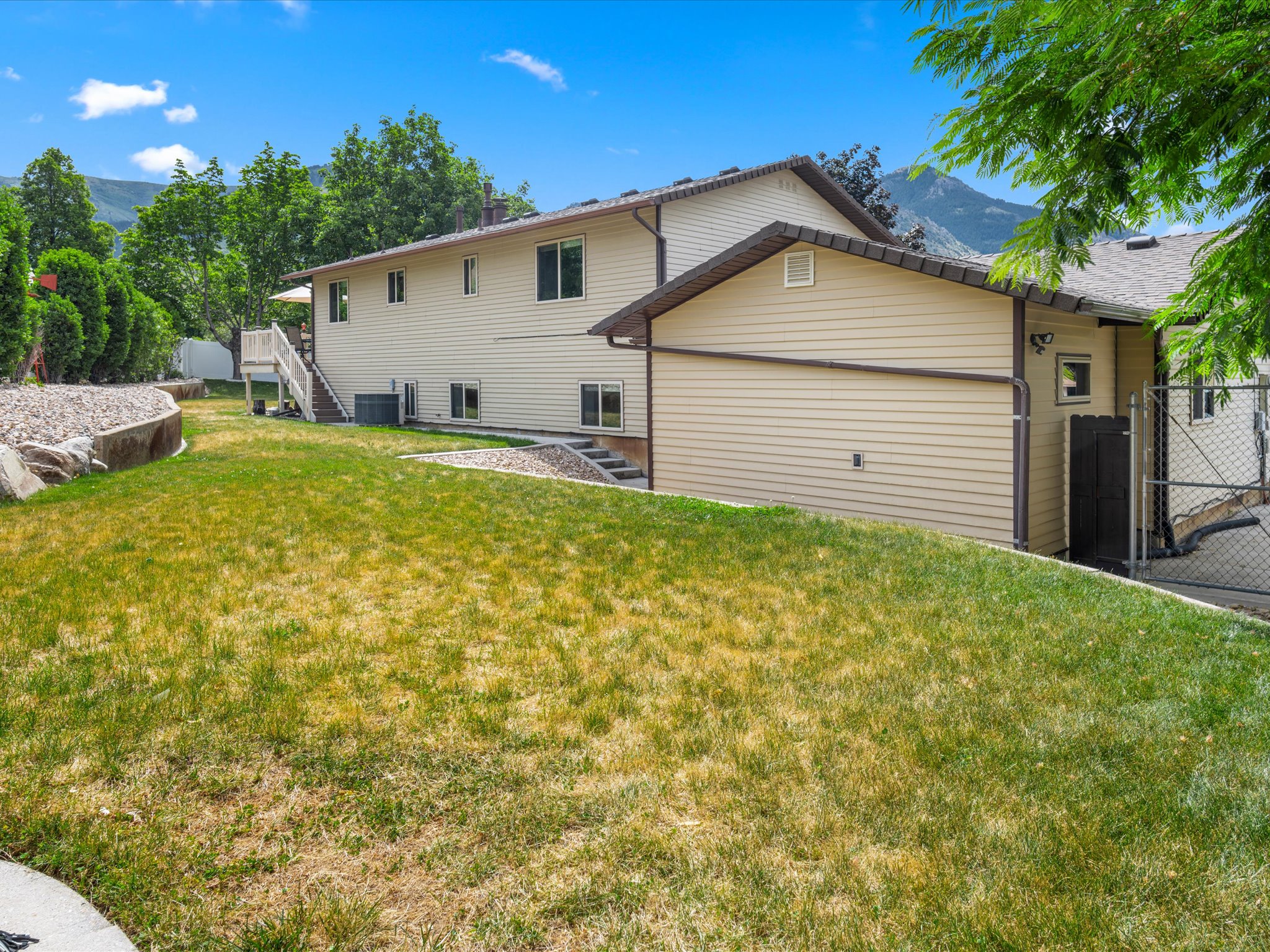 Expansive backyard featuring a large grassy area, a deck with stairs, mature trees, and a mountain backdrop. The shed has power.