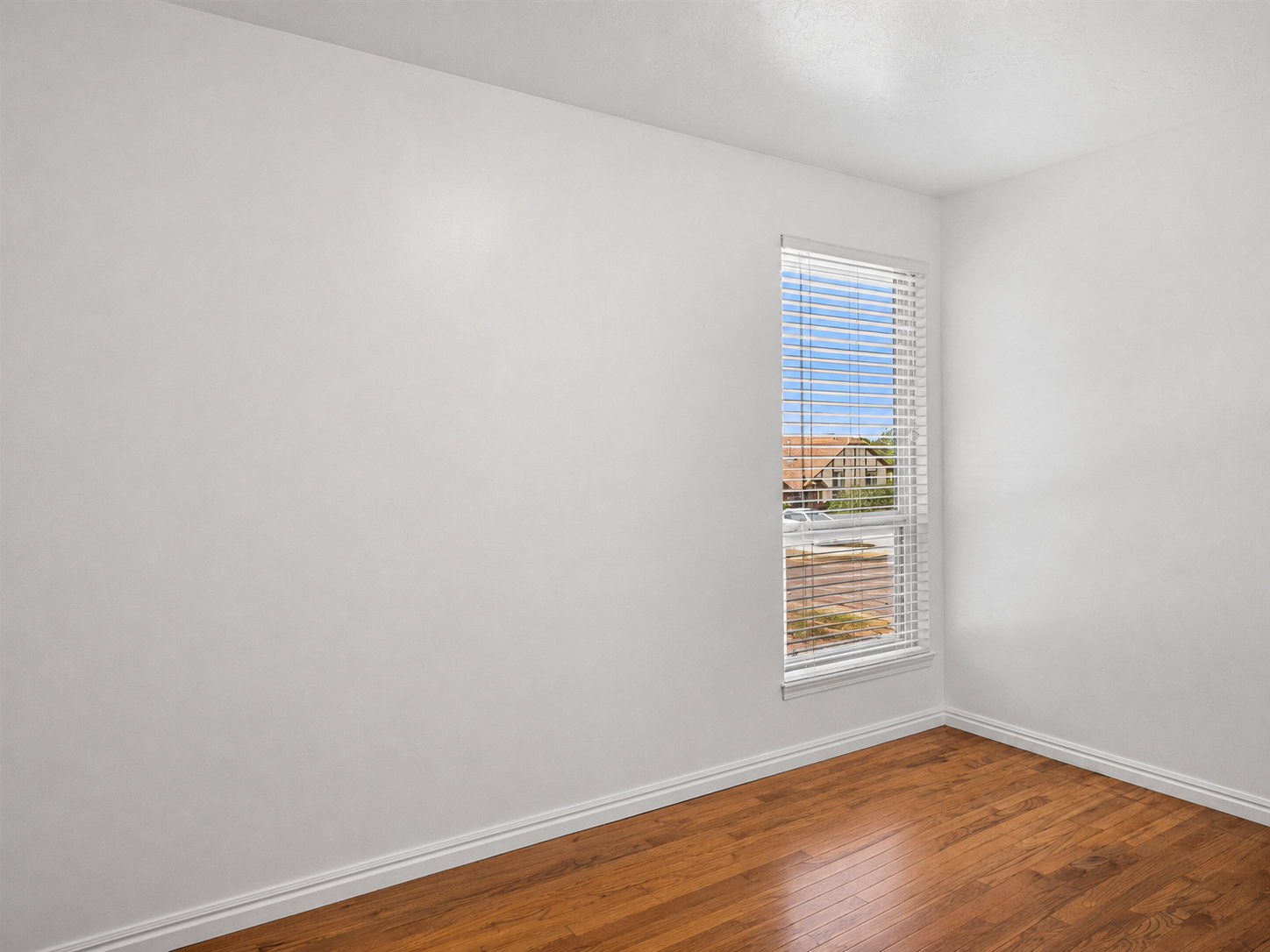 Bright room featuring a single window with blinds, wood flooring, white baseboards, and neutral wall tones