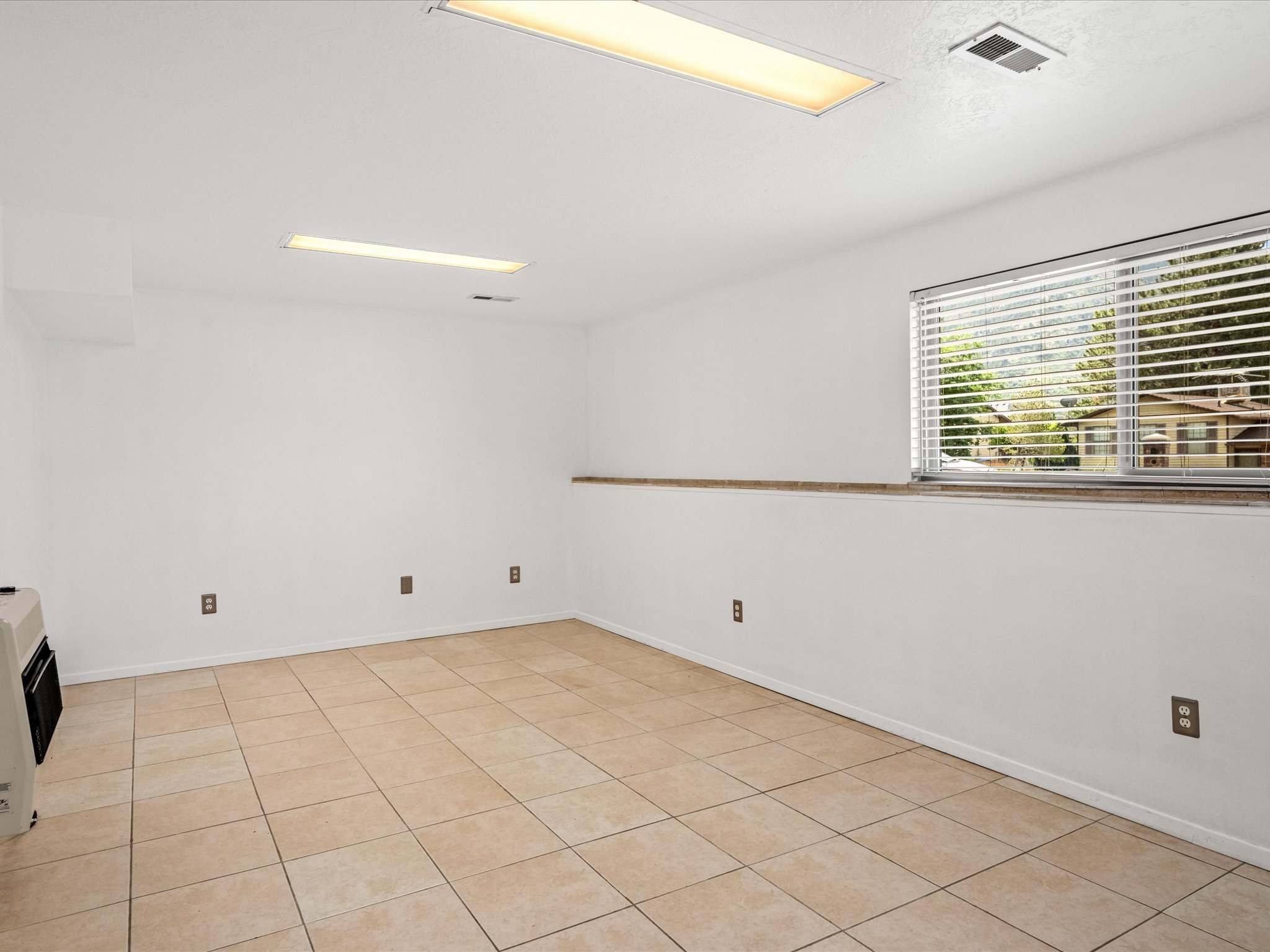 Family room featuring tiled flooring, a window with blinds, and white walls. A removable wall heater is included, but there is forced air.