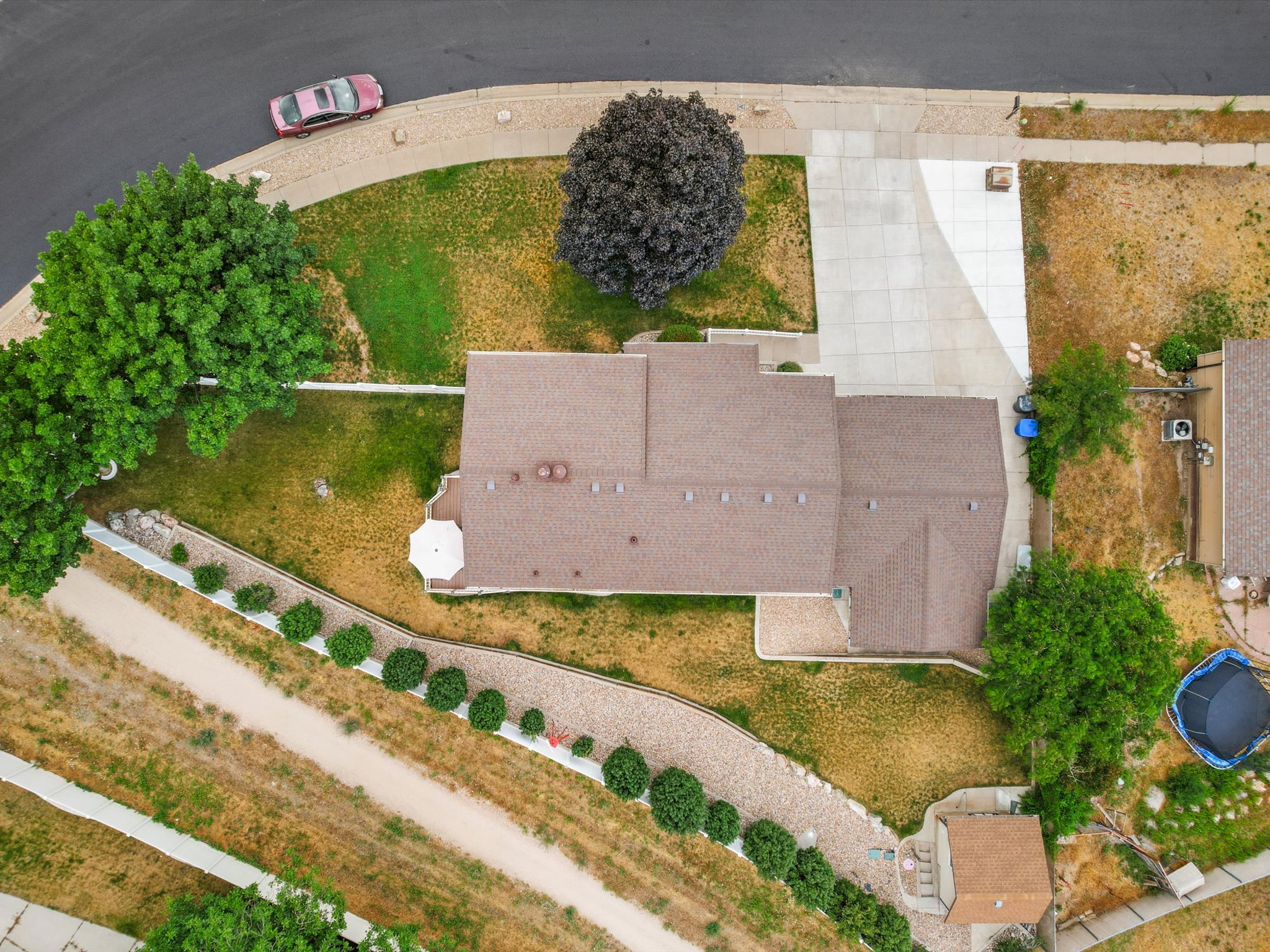 Aerial view showcasing the property's roofline, concrete driveway, and surrounding landscape with the canal trail directly behind the home's fence.