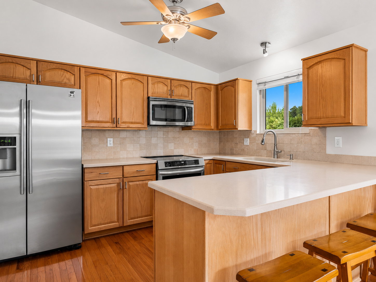 Kitchen featuring wood-finish cabinetry, stainless steel appliances, a tile backsplash, light-toned countertops, and wood flooring