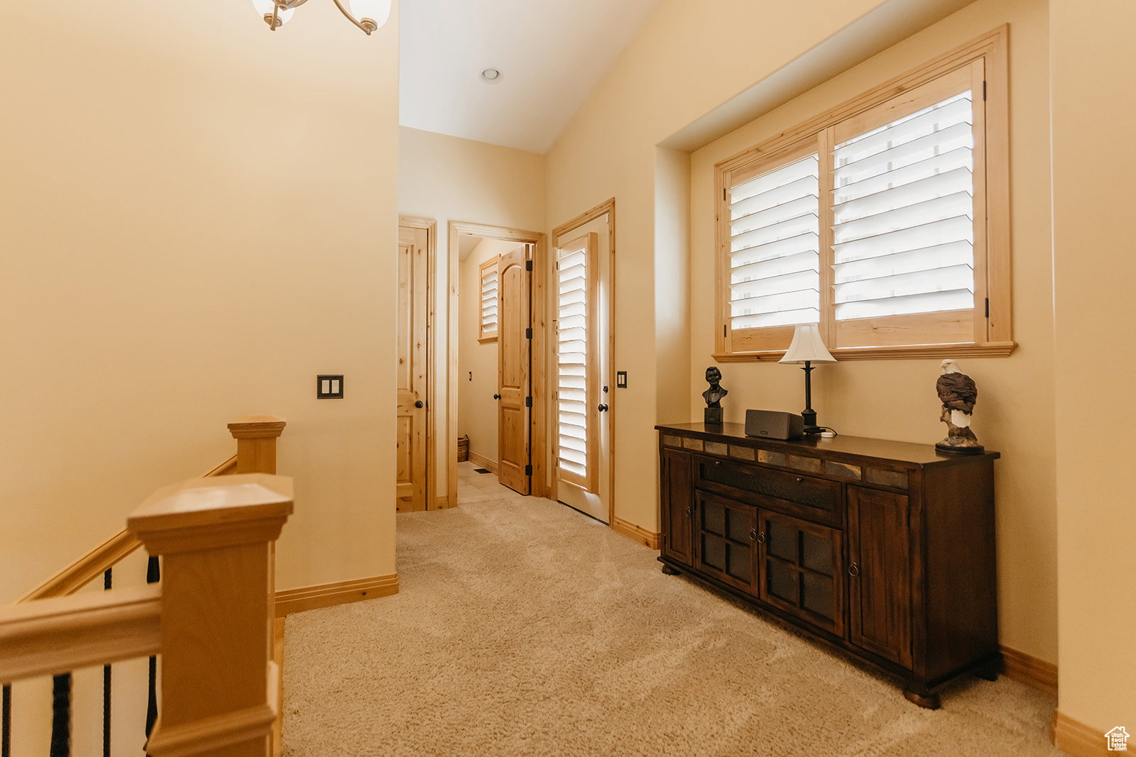 Second-story landing featuring a window with natural wood plantation shutters, light beige carpeting, and natural wood baseboards