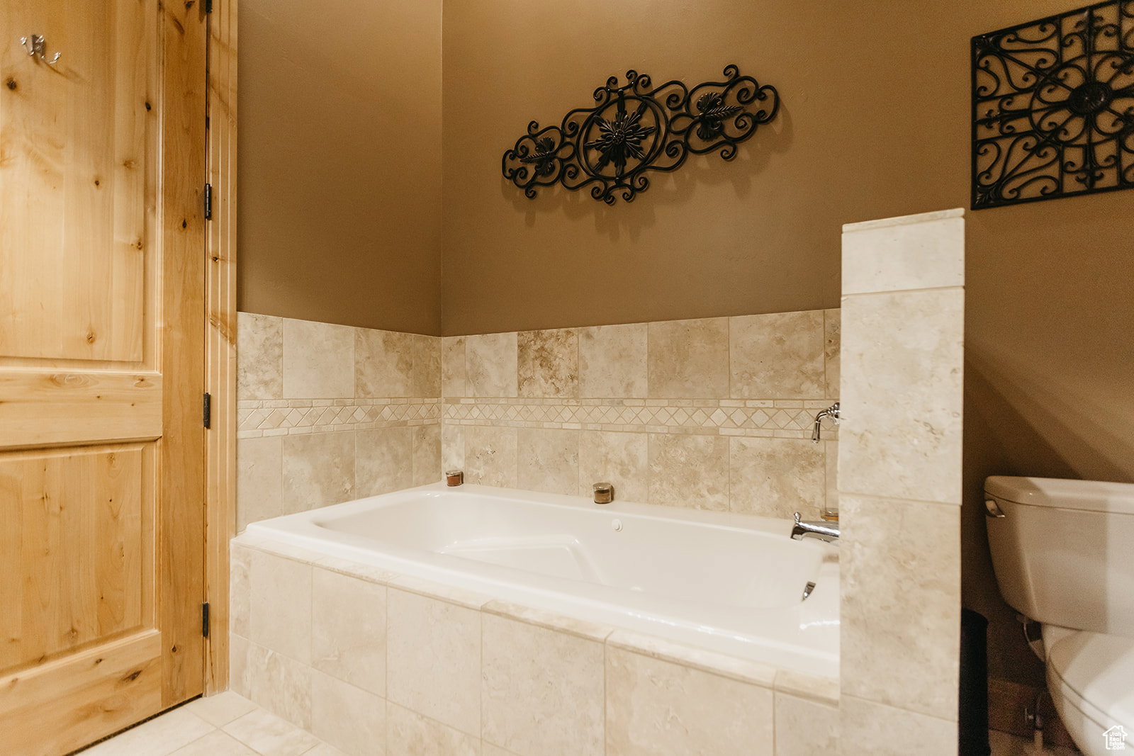 Built-in soaking tub with tile surround, decorative tile accent band, and chrome fixtures