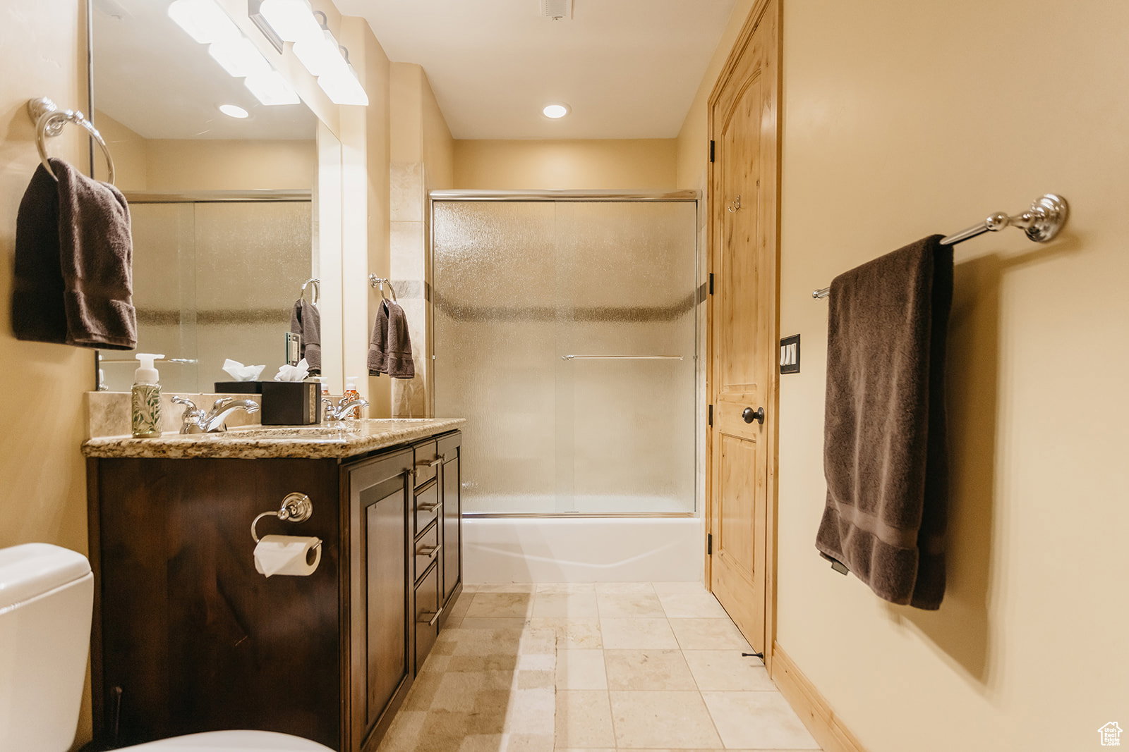 Bathroom featuring a dark wood vanity with a granite countertop, a double sink with chrome fixtures, and a shower-tub combination with a sliding glass door