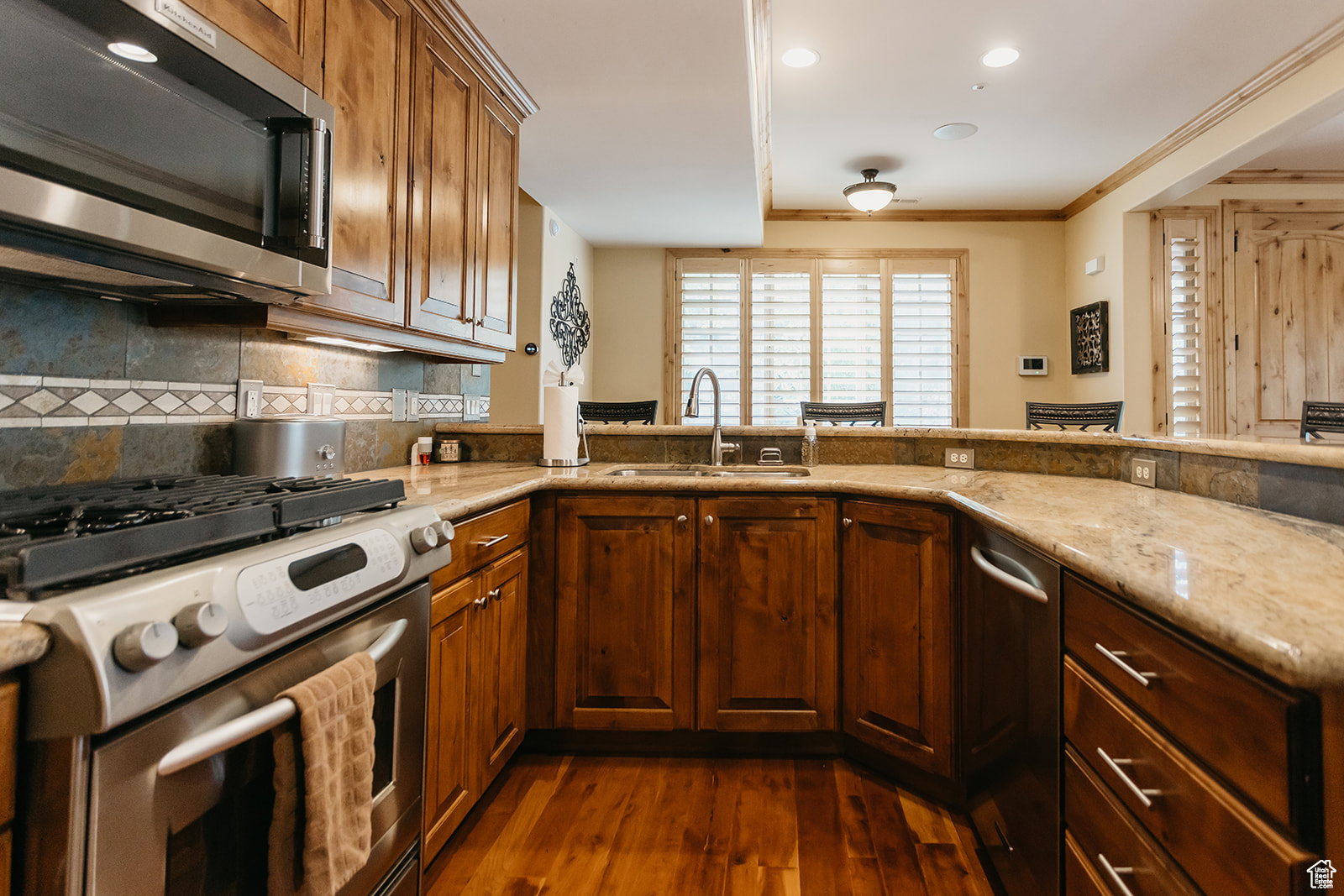Kitchen featuring a stainless steel range and microwave, wood-finish flooring, stone countertops, and wood cabinetry