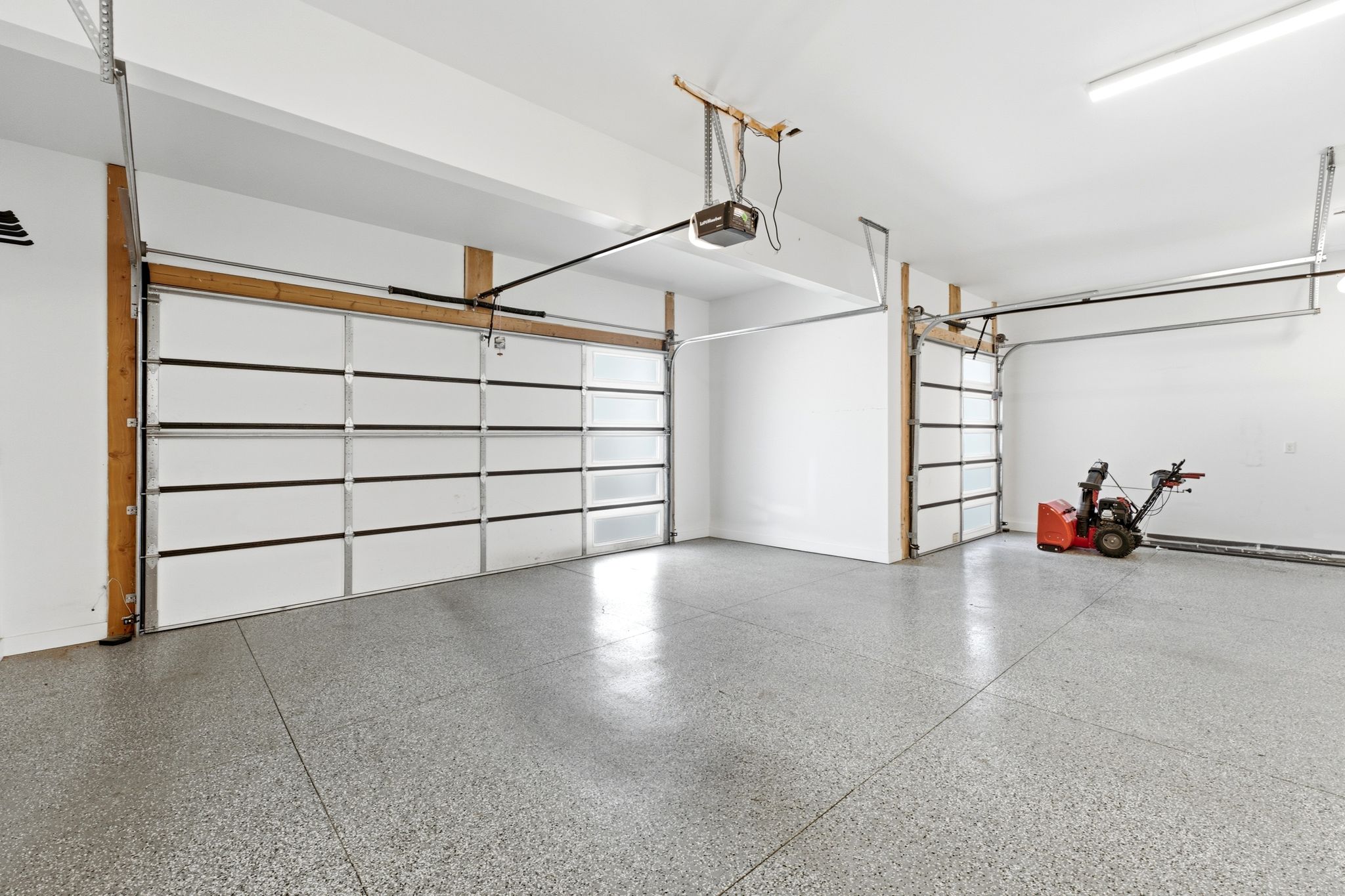 Spacious garage featuring two overhead doors, a light gray epoxy floor, and ceiling-mounted fluorescent lighting