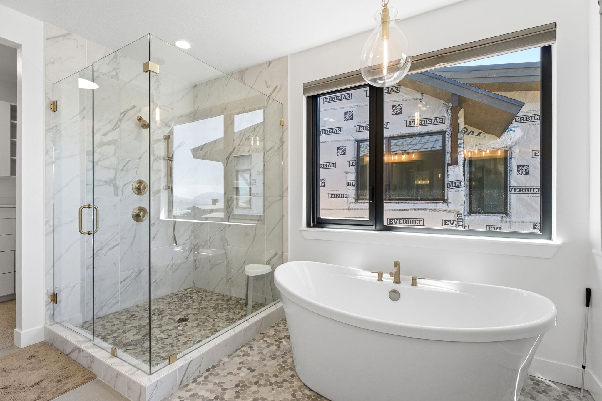 Freestanding soaking tub with gold-finish fixtures and a large picture window