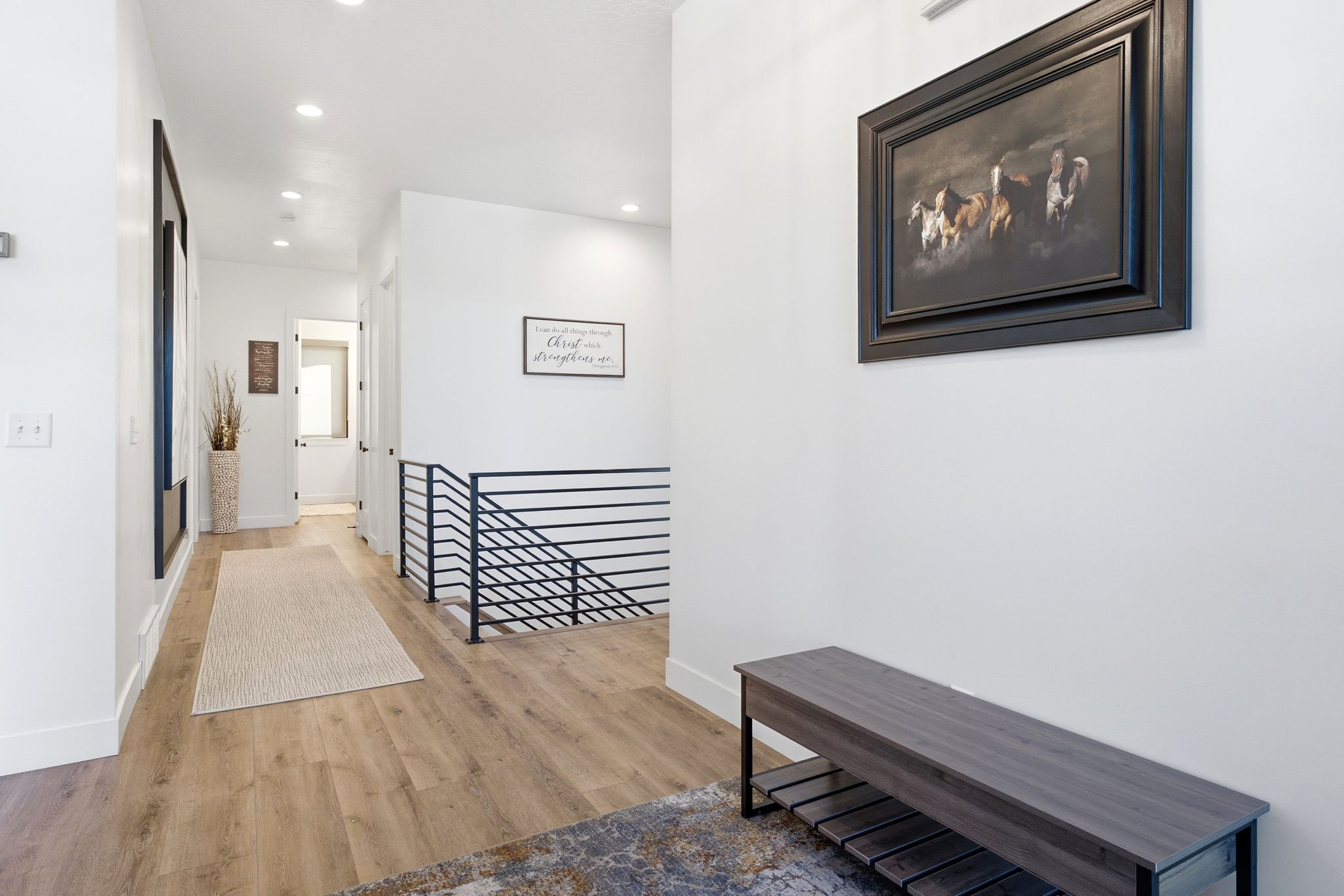Hallway featuring wood-finish flooring, recessed lighting, white walls, and a contemporary black metal stair railing