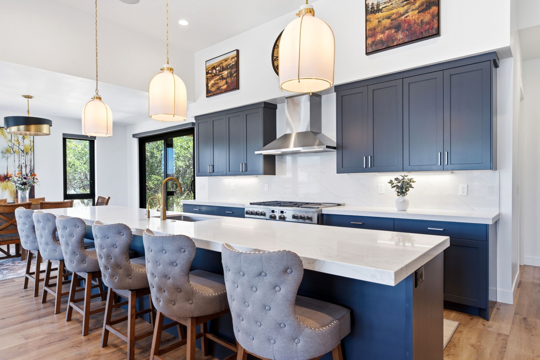 Gourmet kitchen featuring a large central island with seating, dark blue cabinetry, white countertops with matching backsplash, stainless steel range with hood, and wood-finish flooring