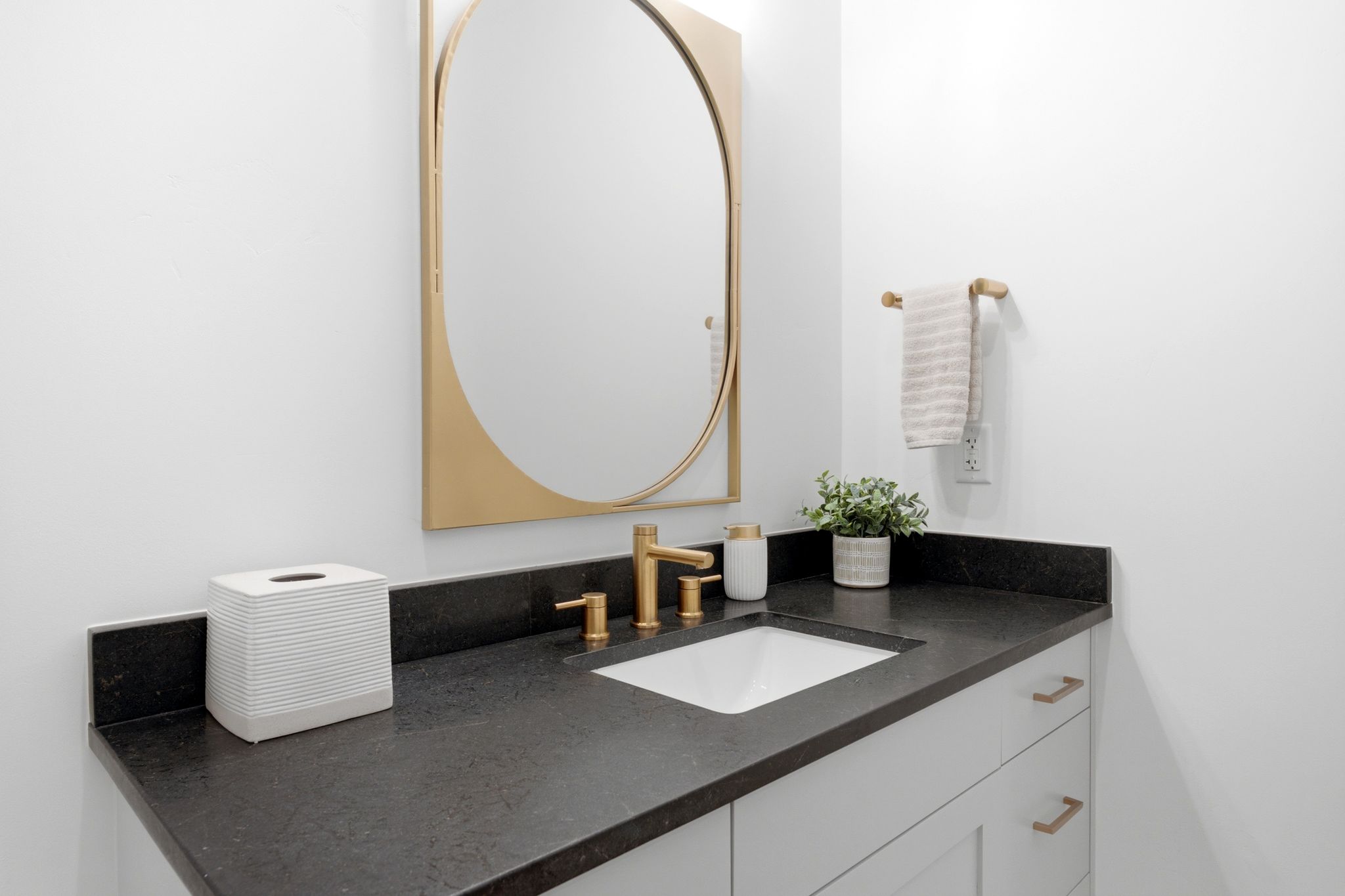 Vanity featuring a dark countertop, undermount sink, and brass-finish faucet